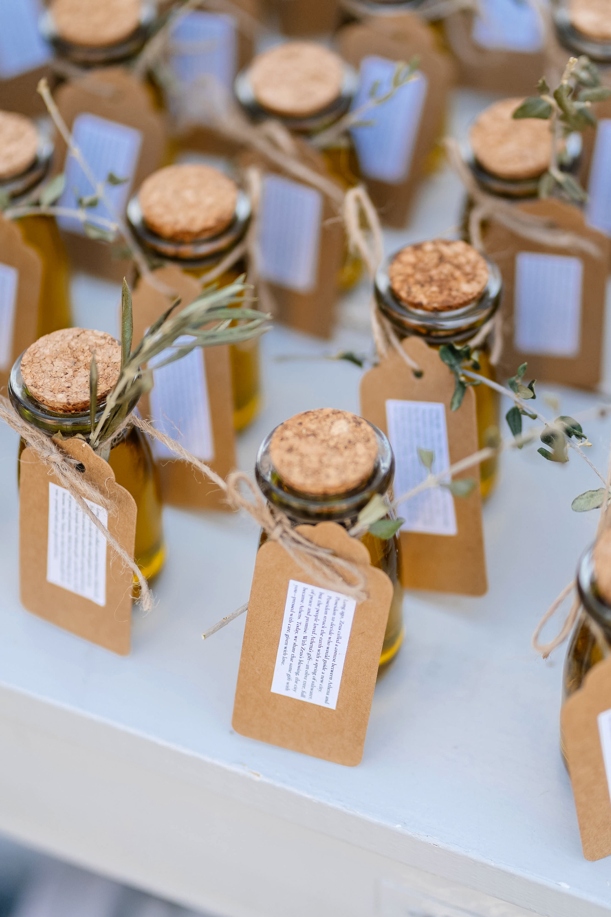 Multiple small glass bottles with cork stoppers, tied with twine and labeled with brown paper tags, decorated with sprigs of greenery.