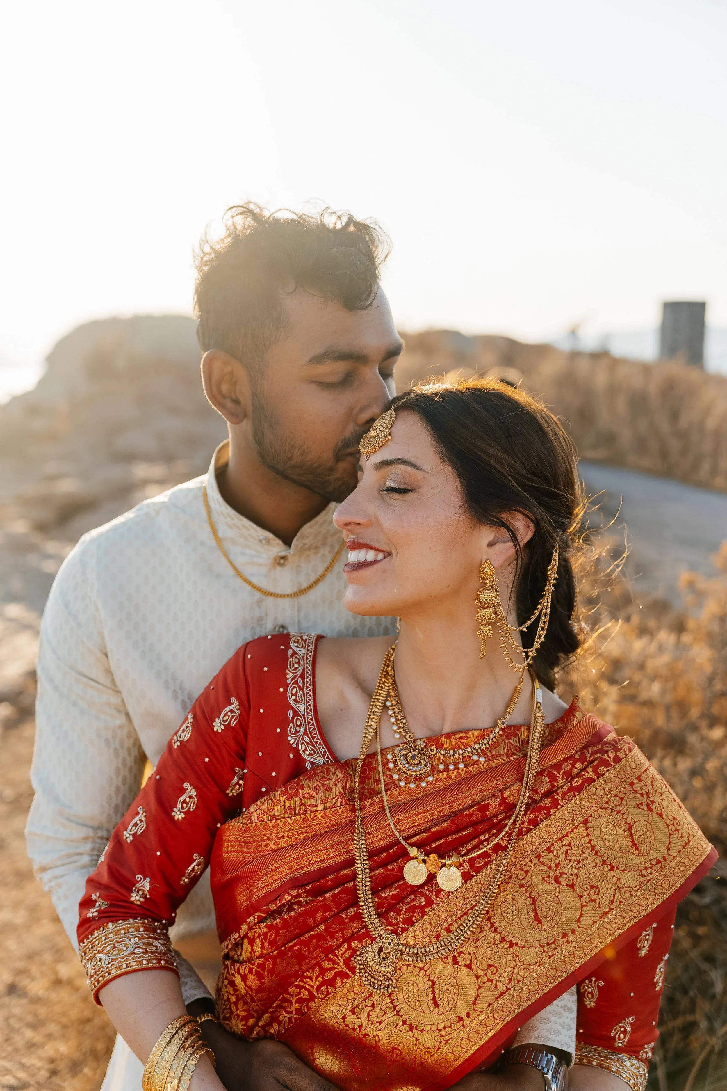 A romantic moment between a couple dressed in traditional Indian attire outdoors in a sunny setting.