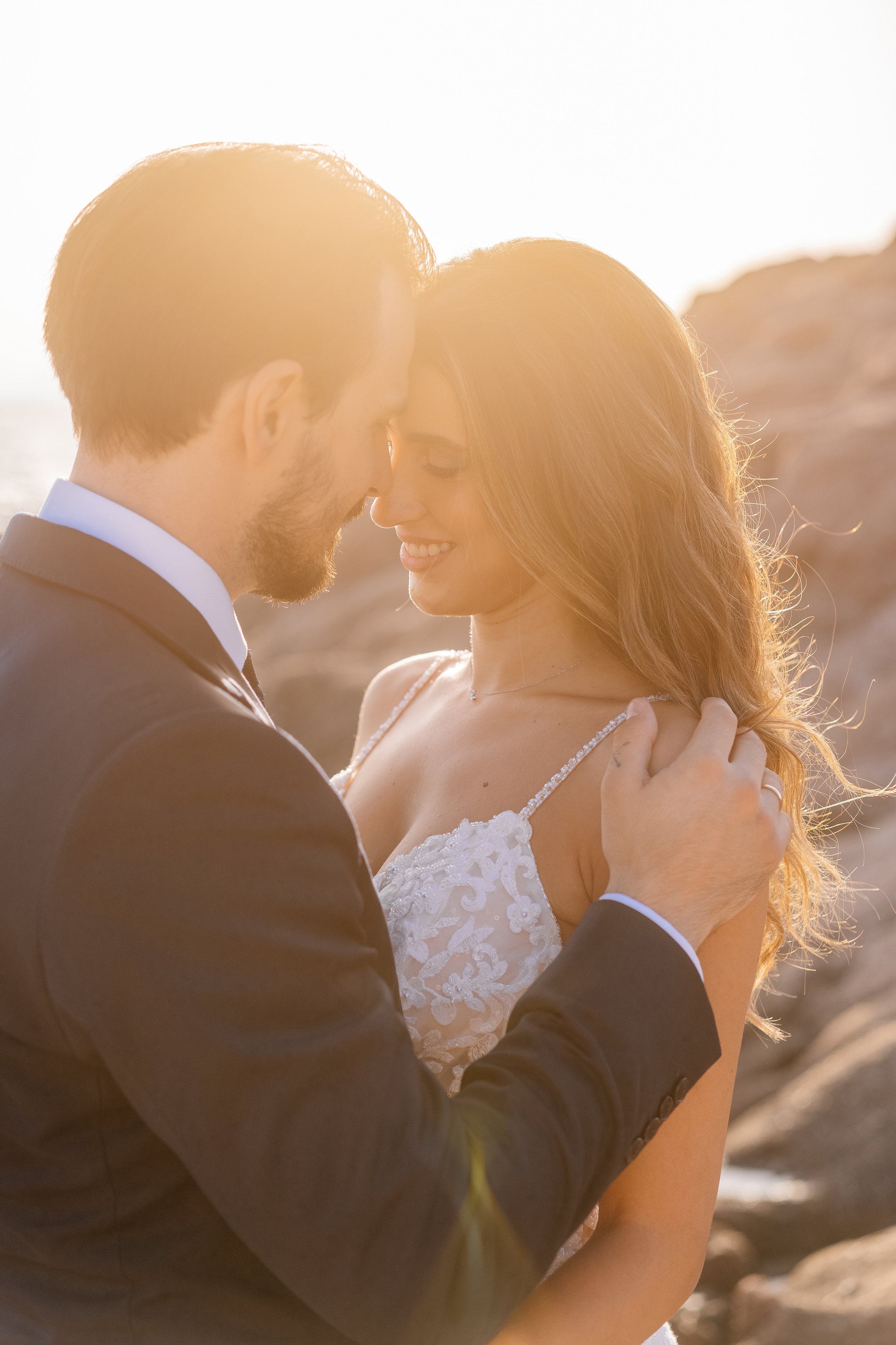 A couple sharing an intimate moment outdoors at sunset, with the man in a suit and the woman in a wedding dress.