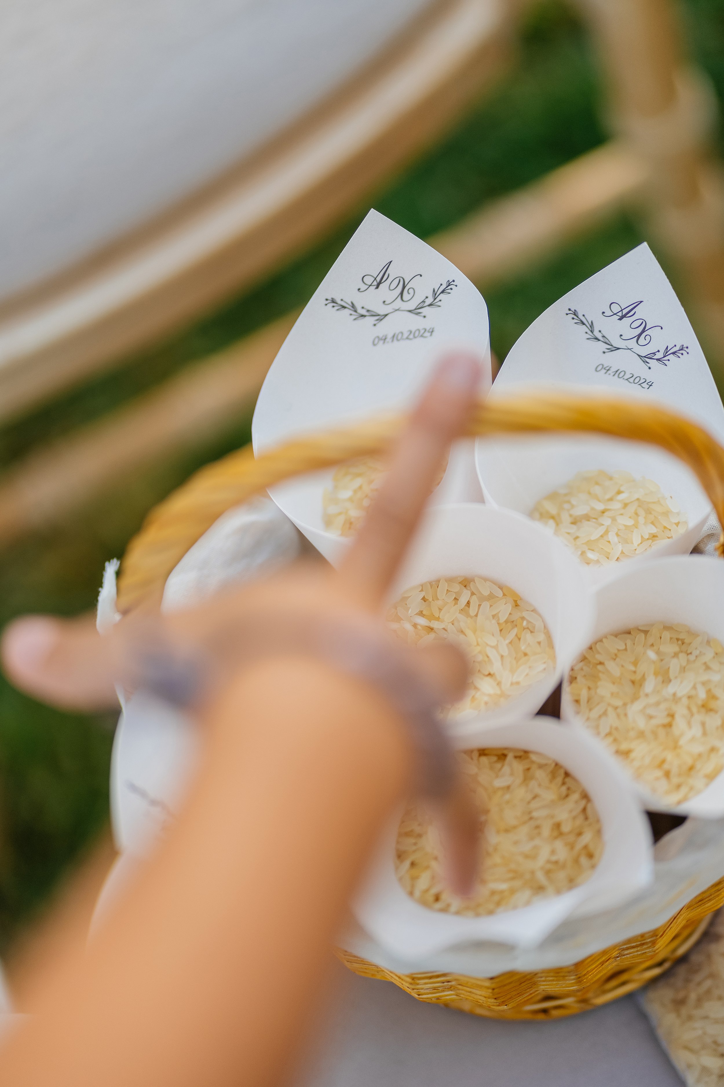 Close-up of a basket of rice with two white cards that have decorative writing and the date 04.10.2024, held by a person's hand.
