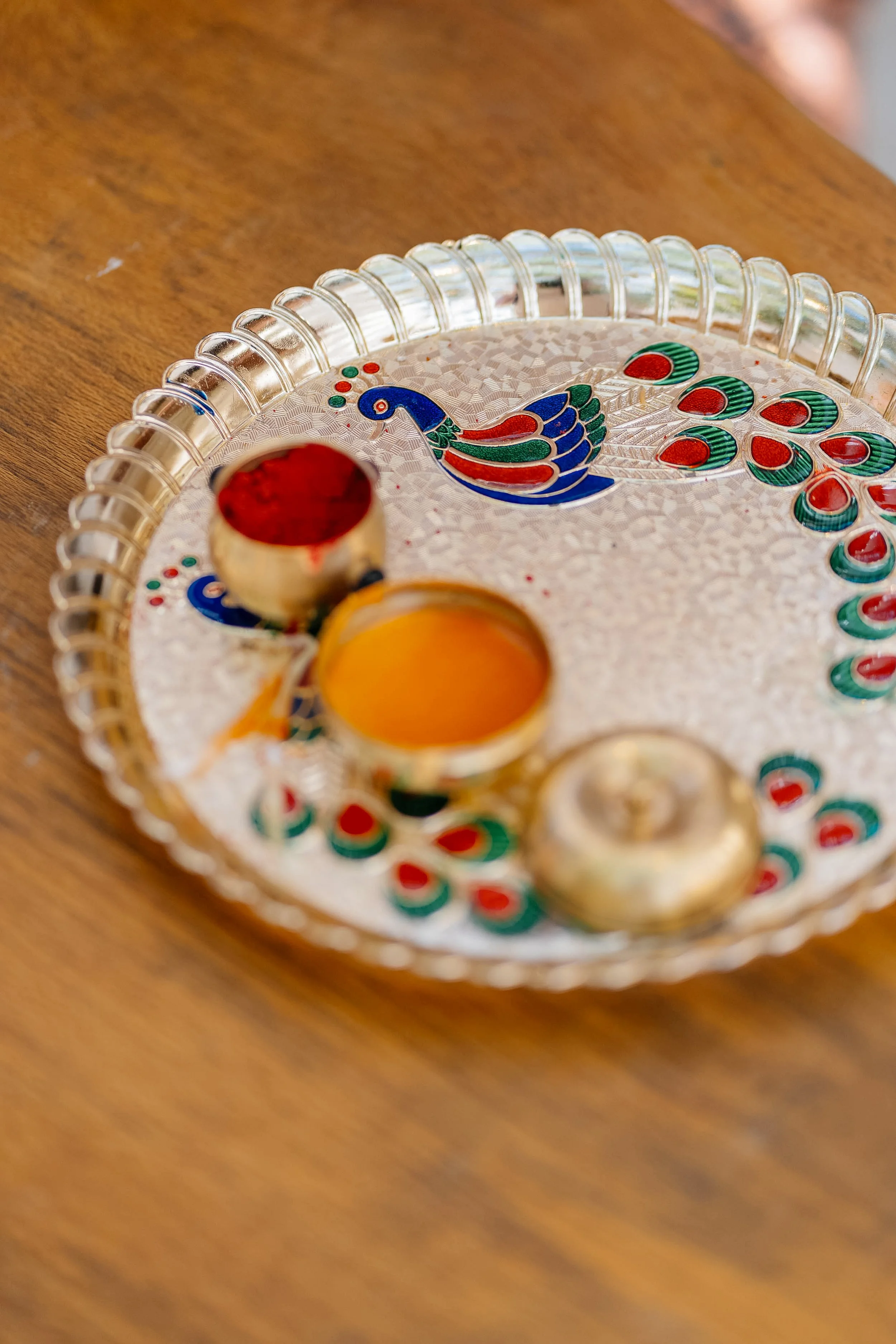 Close-up of a decorative glass tray with a colorful peacock design, placed on a wooden surface.