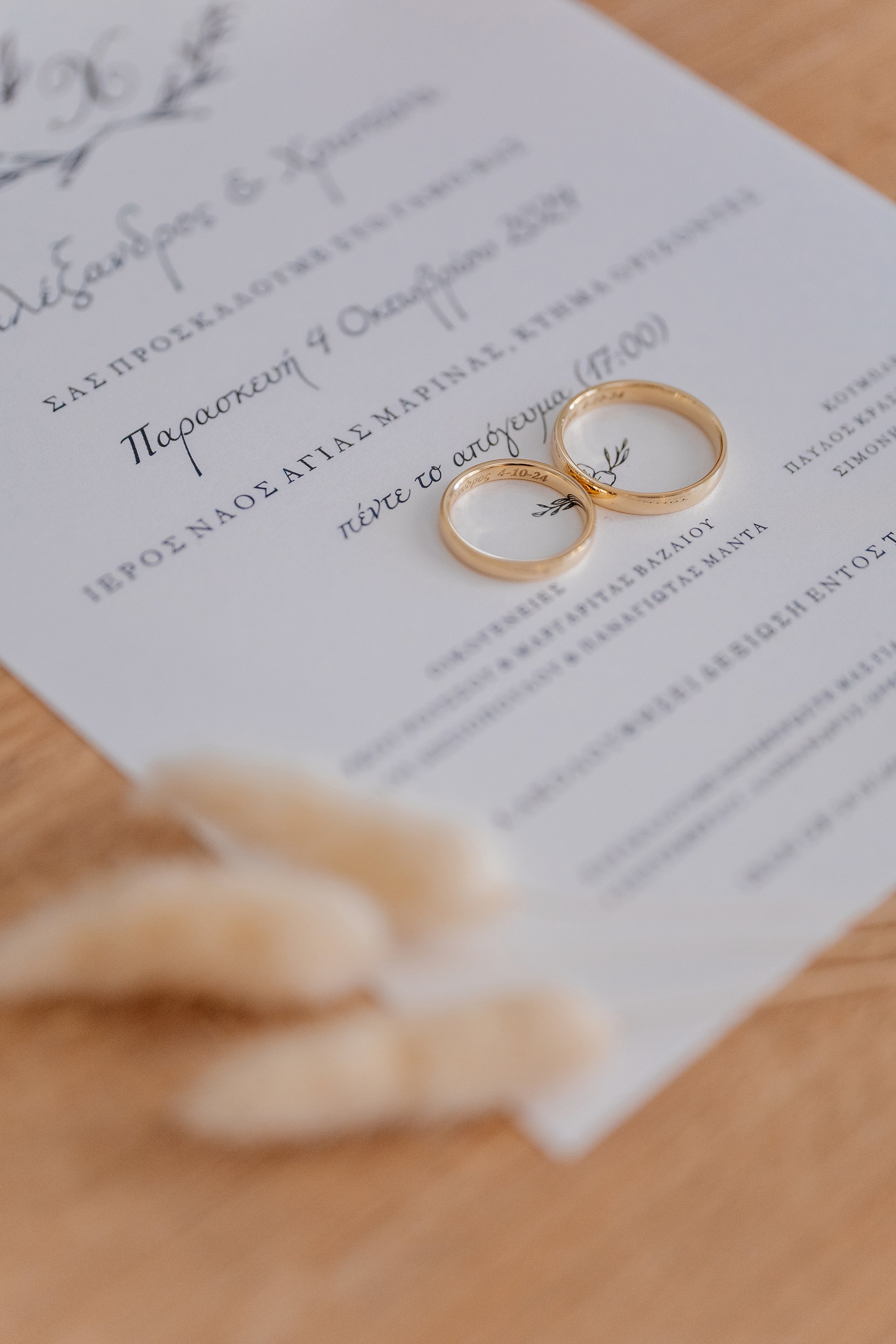 Close-up of two gold wedding rings placed on a wedding invitation with decorative text and floral accents.
