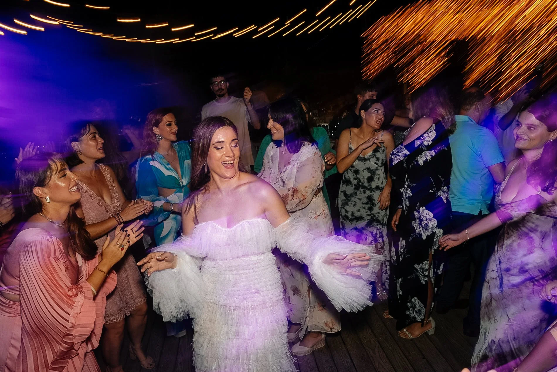 People dancing at a lively party with colorful lighting and string lights overhead.