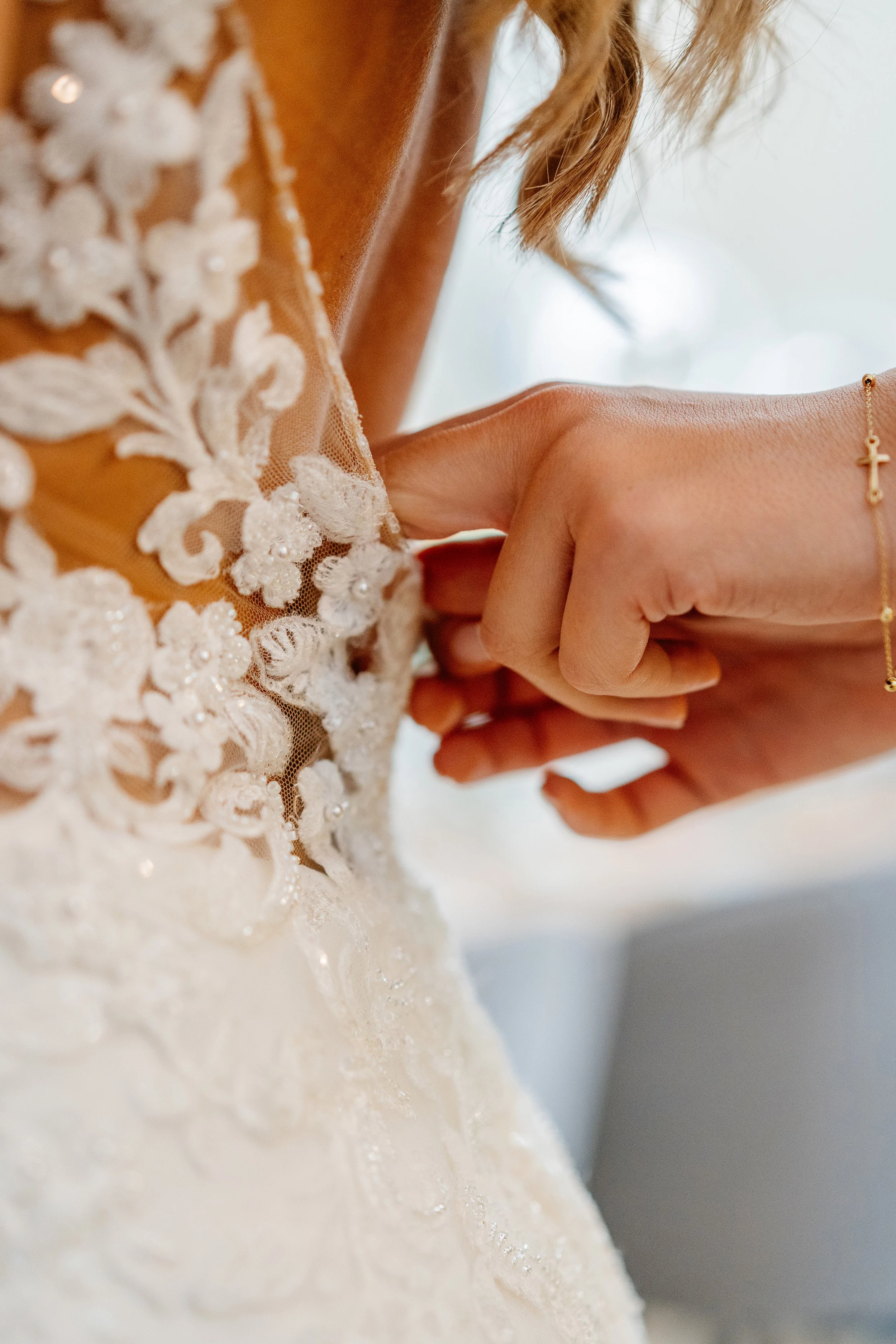 Close-up of a woman adjusting the lace and beaded details on her wedding dress, with a focus on the intricate embroidery and delicate fabric.
