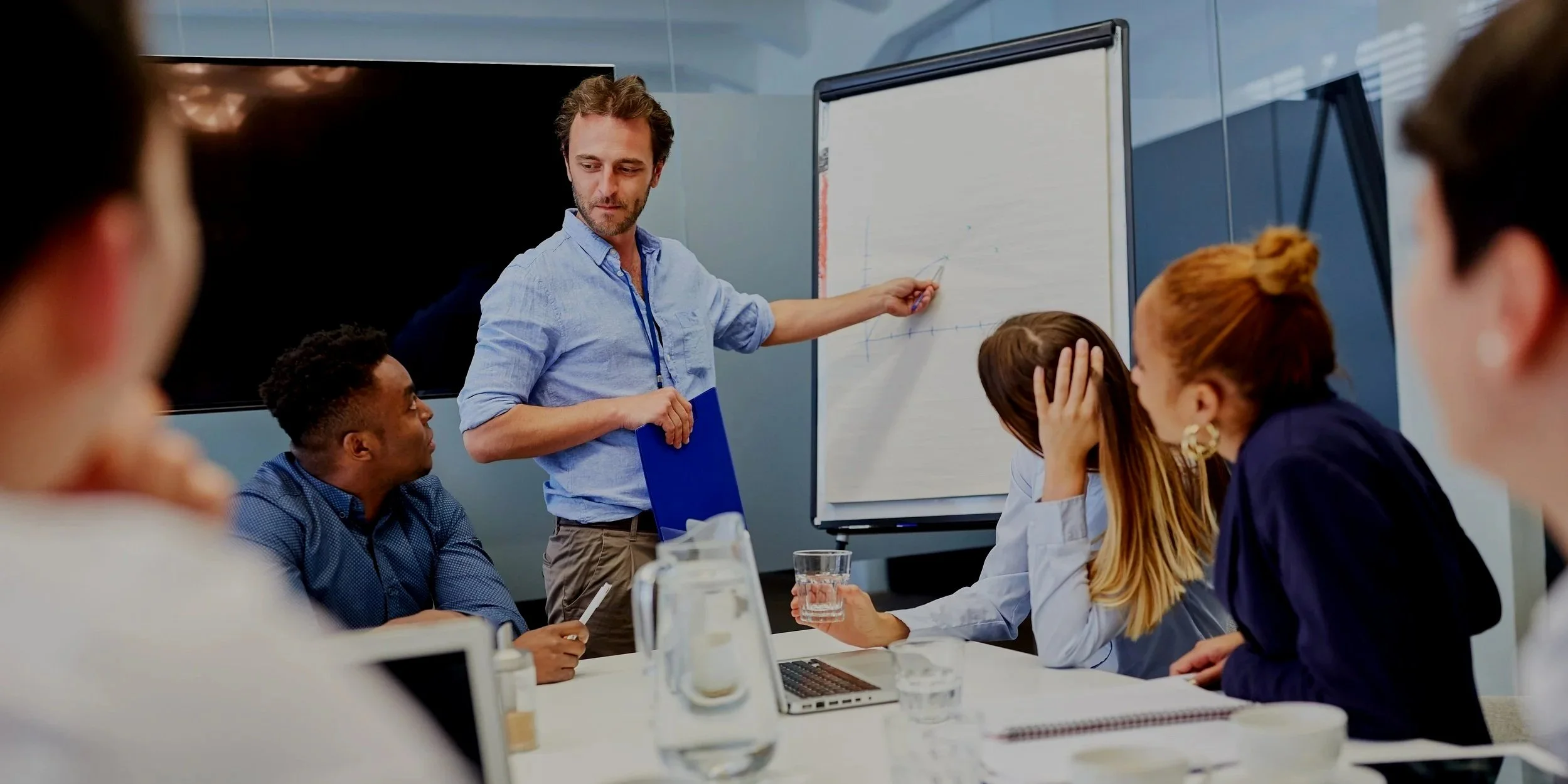 Man giving a presentation to a group of diverse young adults in a conference room.