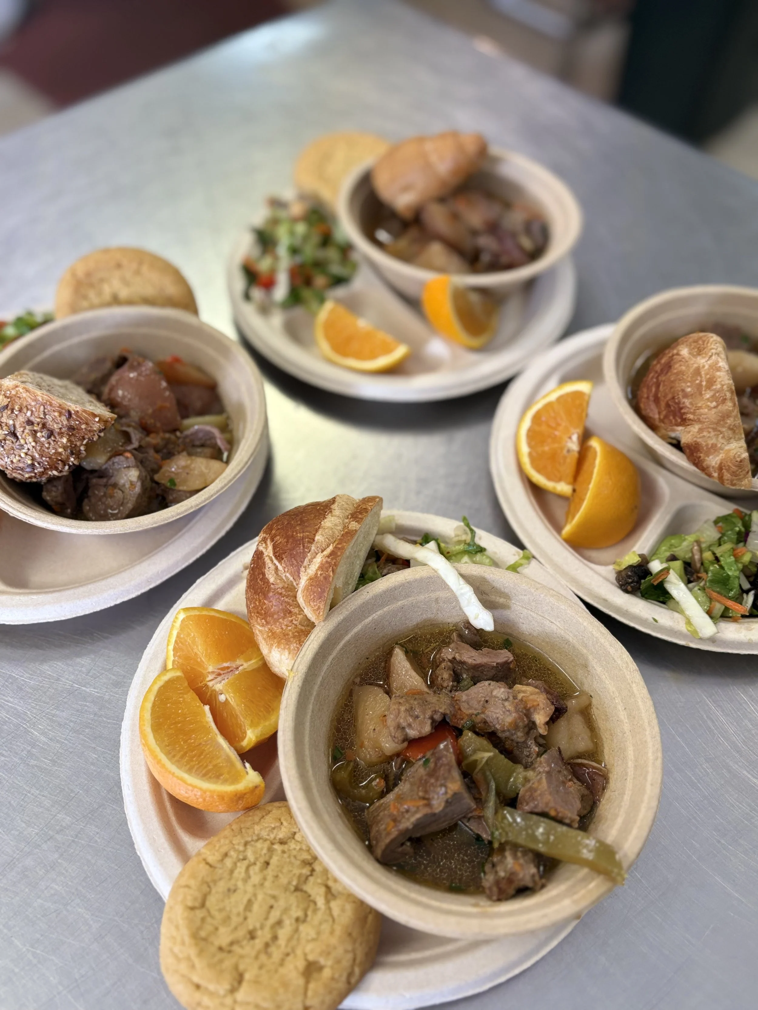 A foam tray with a salad, fruit salad, biscuit, bread roll, and slice of cake.