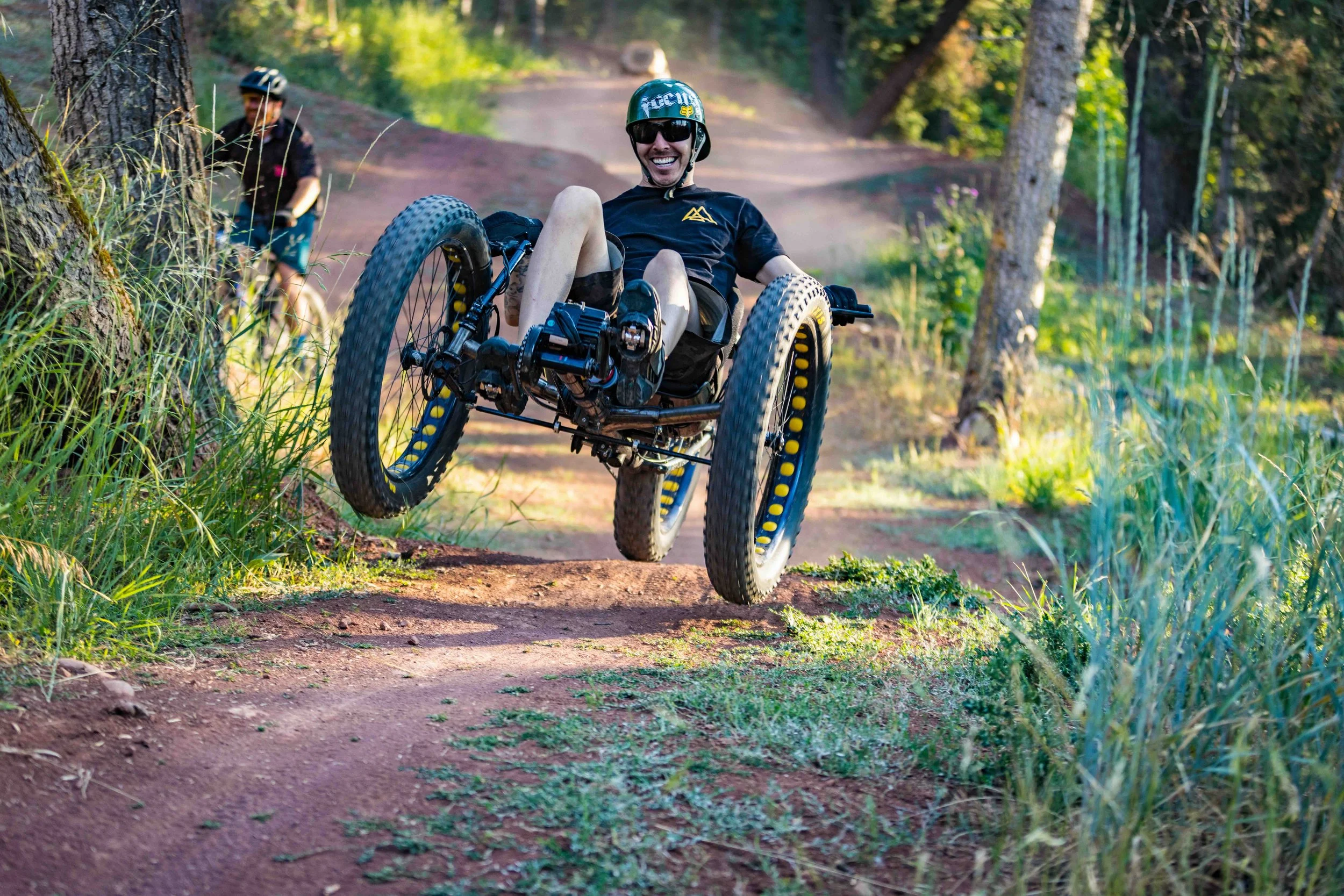 Aaron Baker picking up speed on a dirt trail in a forest, with another person in the background.