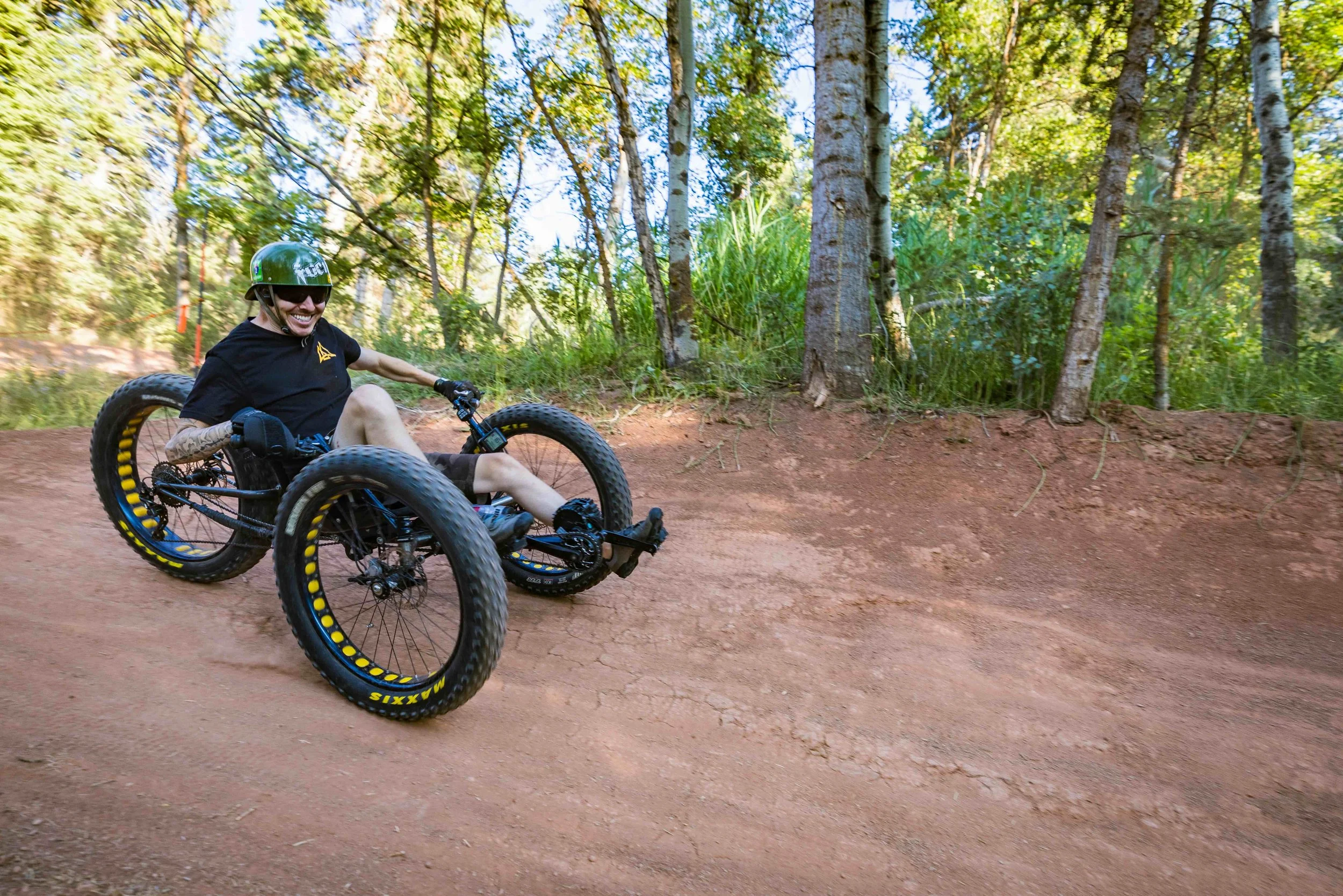 Aaron Baker mountain biking on a dirt trail through a forested area with trees and green foliage.