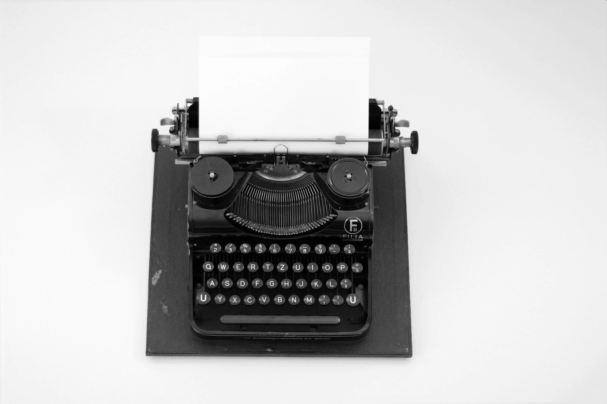 A vintage black manual typewriter with a blank sheet of paper inside, placed on a black surface.