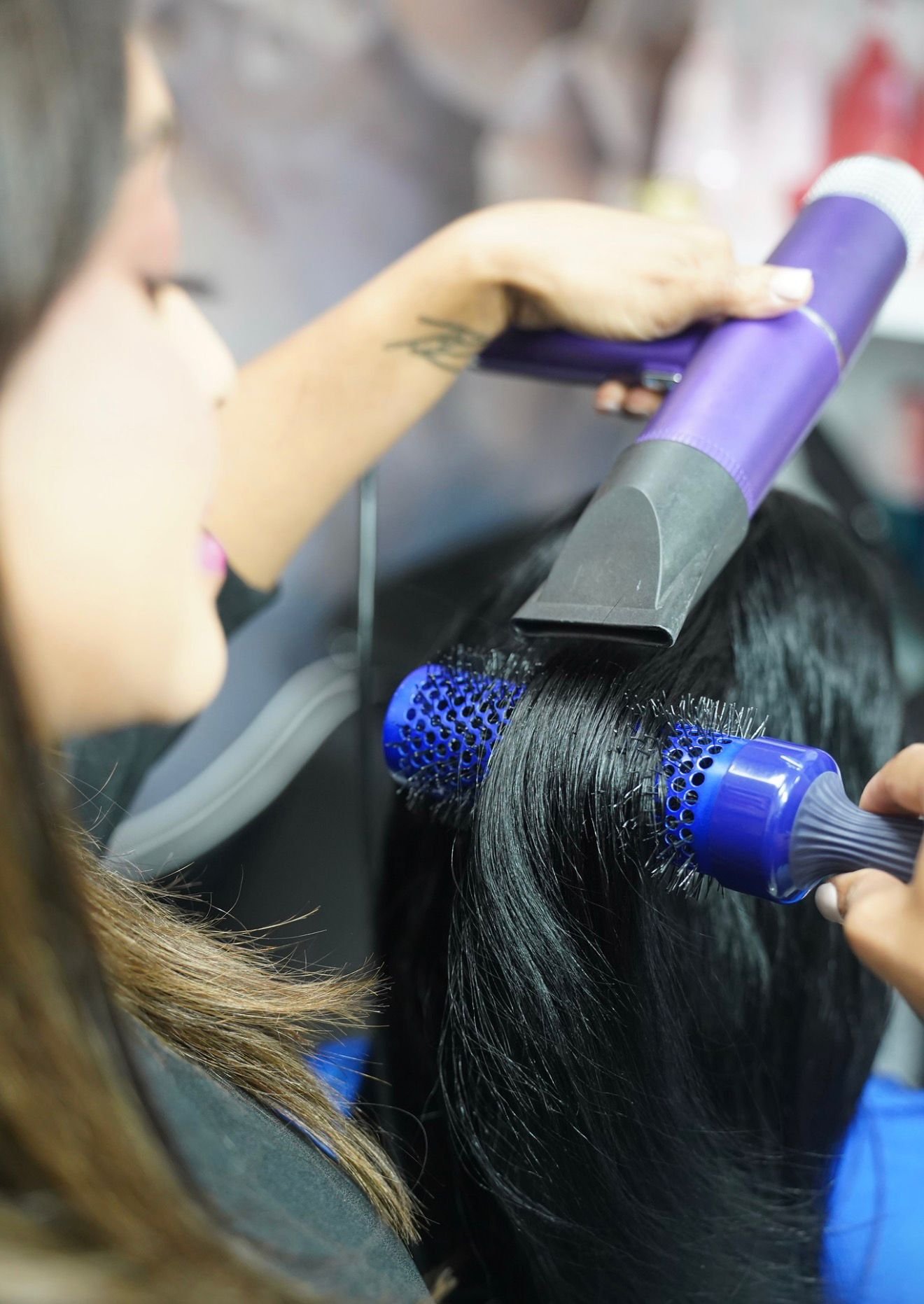 A hairstylist drying a person's hair with a blow dryer and a round brush.