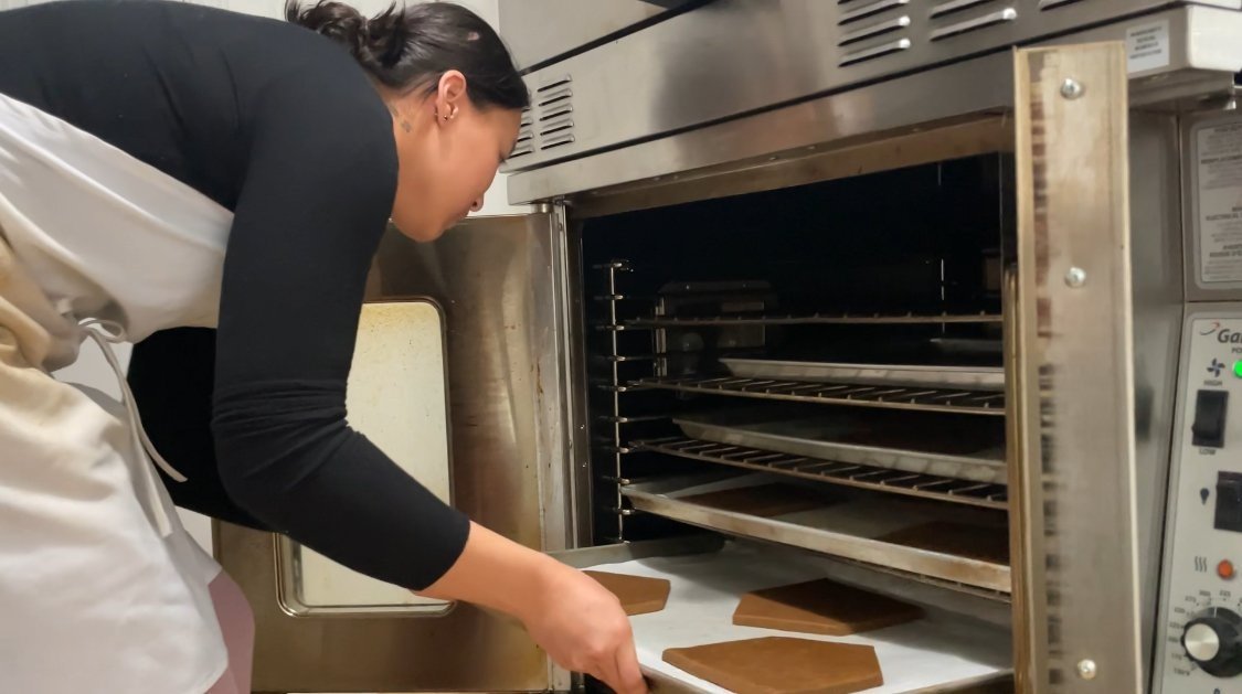 A woman inserting baking sheets into an oven in a commercial kitchen.