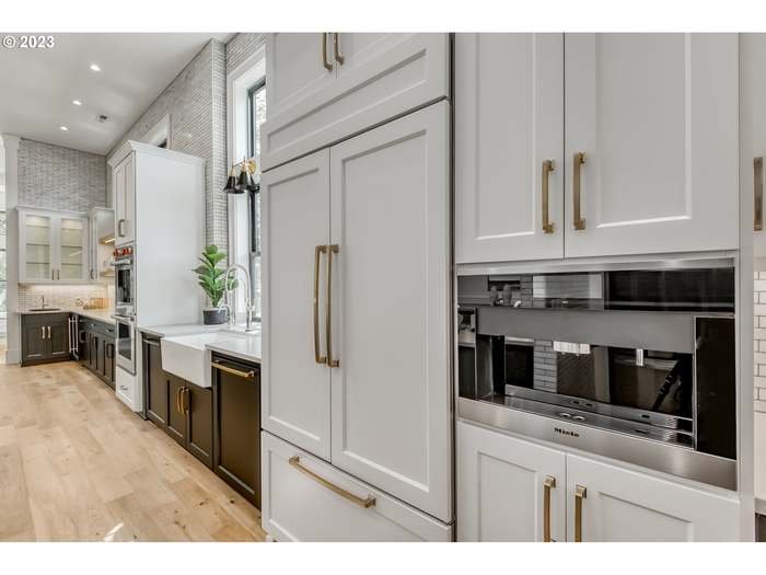 Modern kitchen with white and black cabinetry, built-in coffee maker, large refrigerator, and wooden flooring.