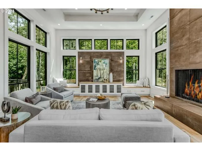 Bright modern living room with large windows, white walls, a fireplace, and contemporary furniture including sofas and armchairs.