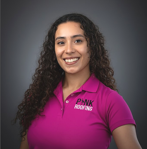 A woman with long curly hair wearing a pink polo shirt with the logo 'PINK ROOFING' smiles at the camera against a dark background.