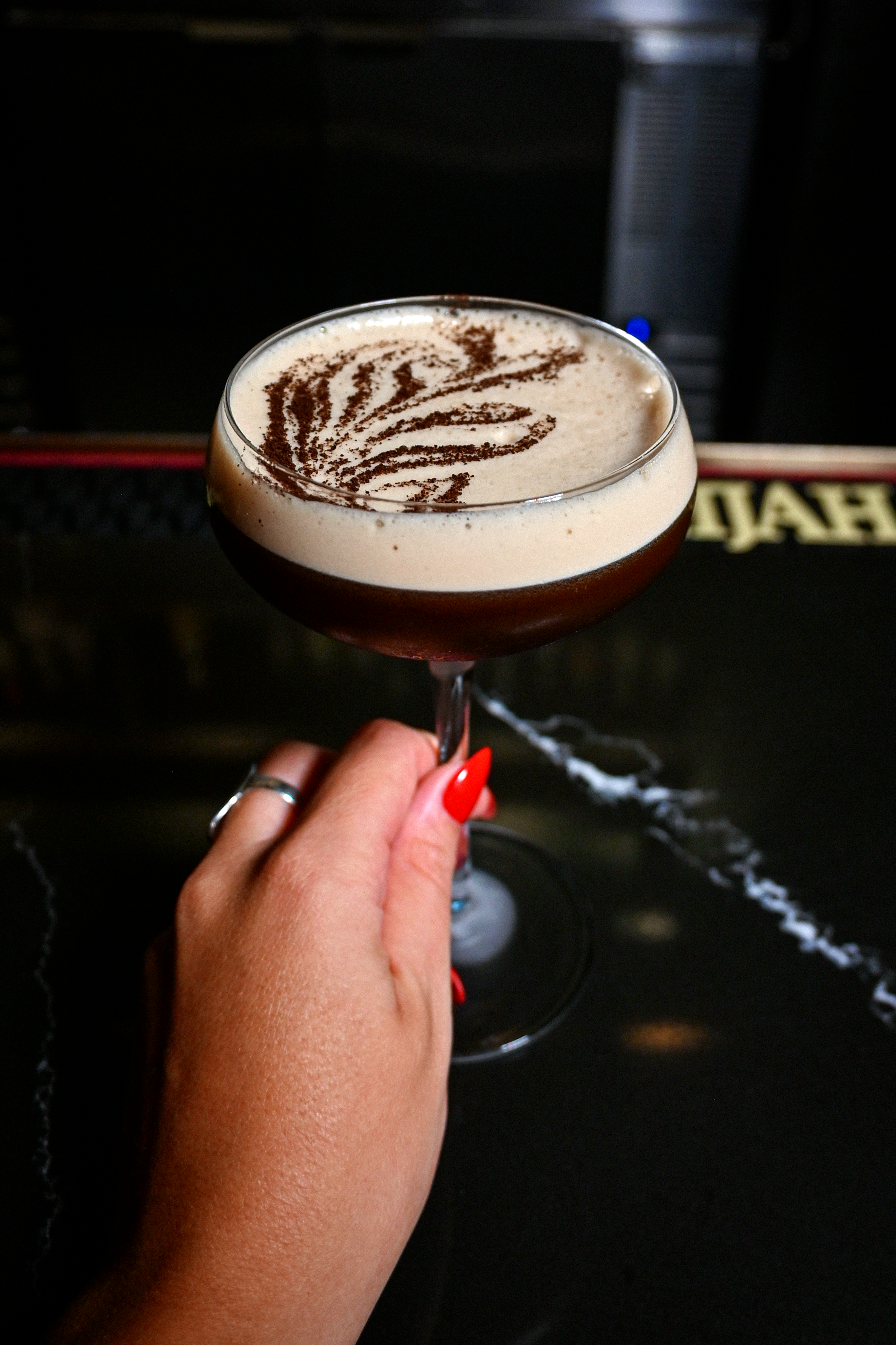 woman's hands with red nails holding espresso martini which is one of the cocktails offered on our menu for private events or full restaurant buyout option in charlotte elizabeth