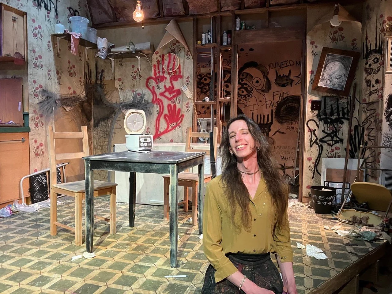 Alex smiles in front of a set on a stage.