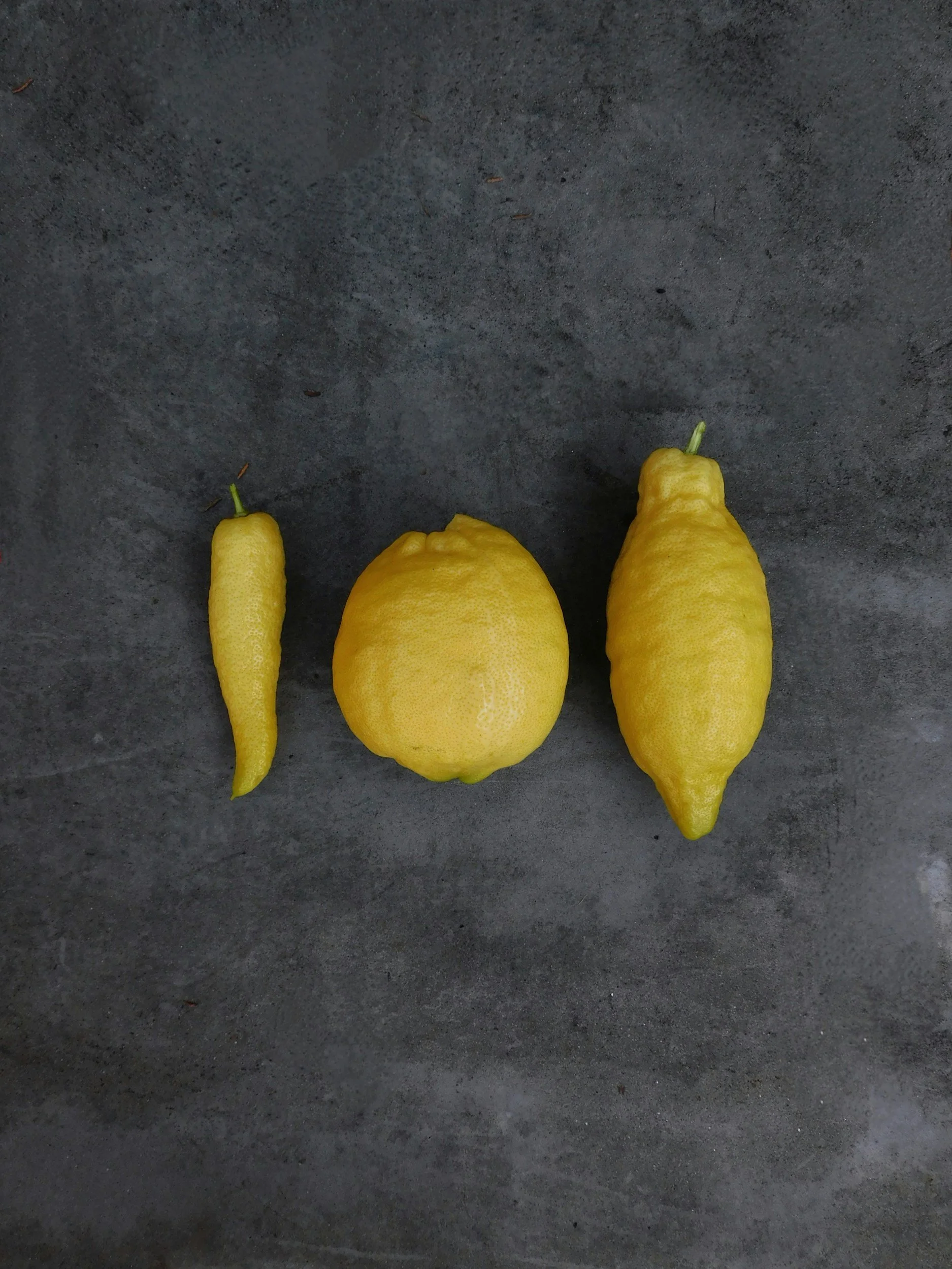 Three yellow lemons placed on a dark gray surface.