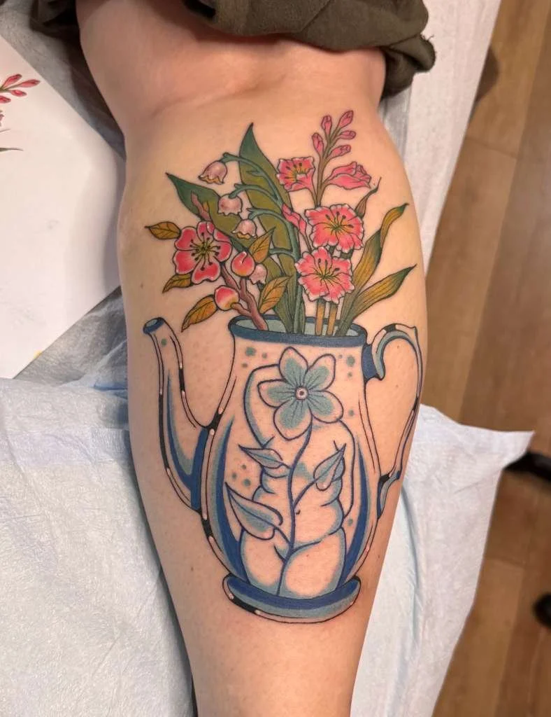 Tattoo of a floral bouquet in a pitcher on a person's thigh.