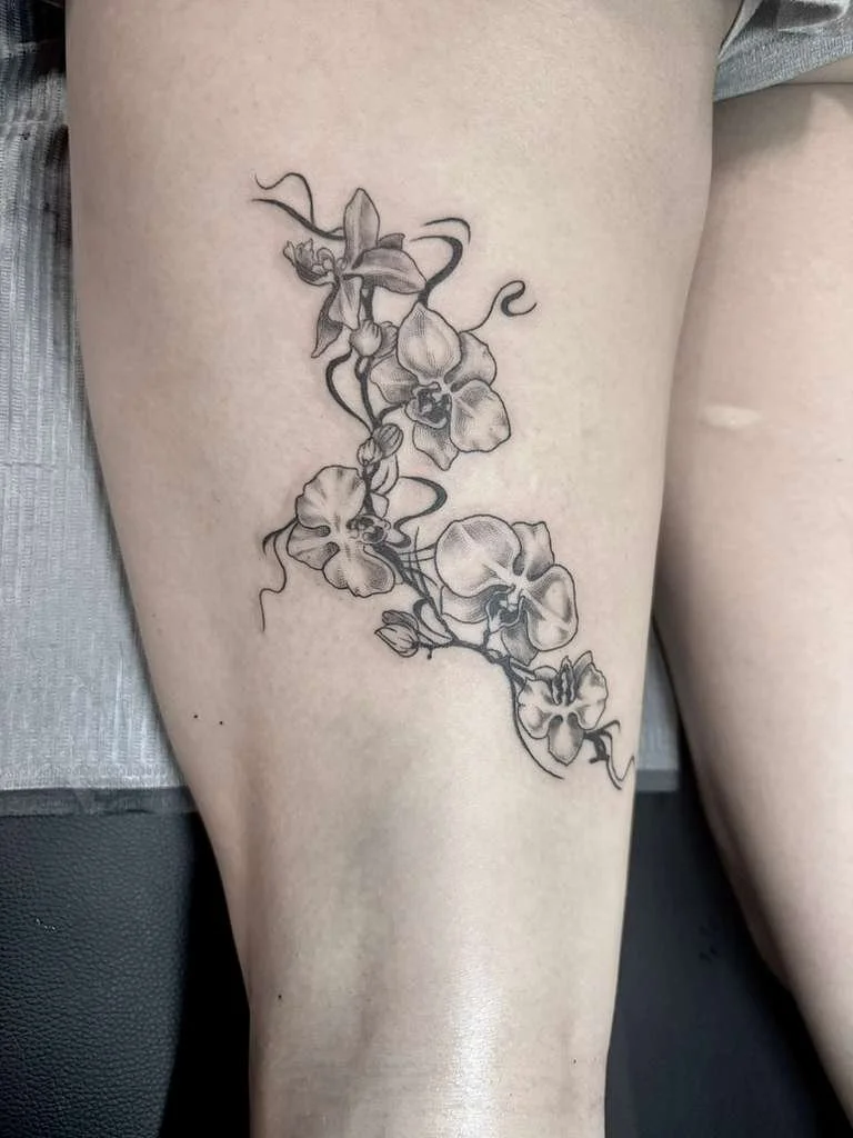 A person's torso with various black ink tattoos, including a butterfly, floral designs, and decorative patterns.
