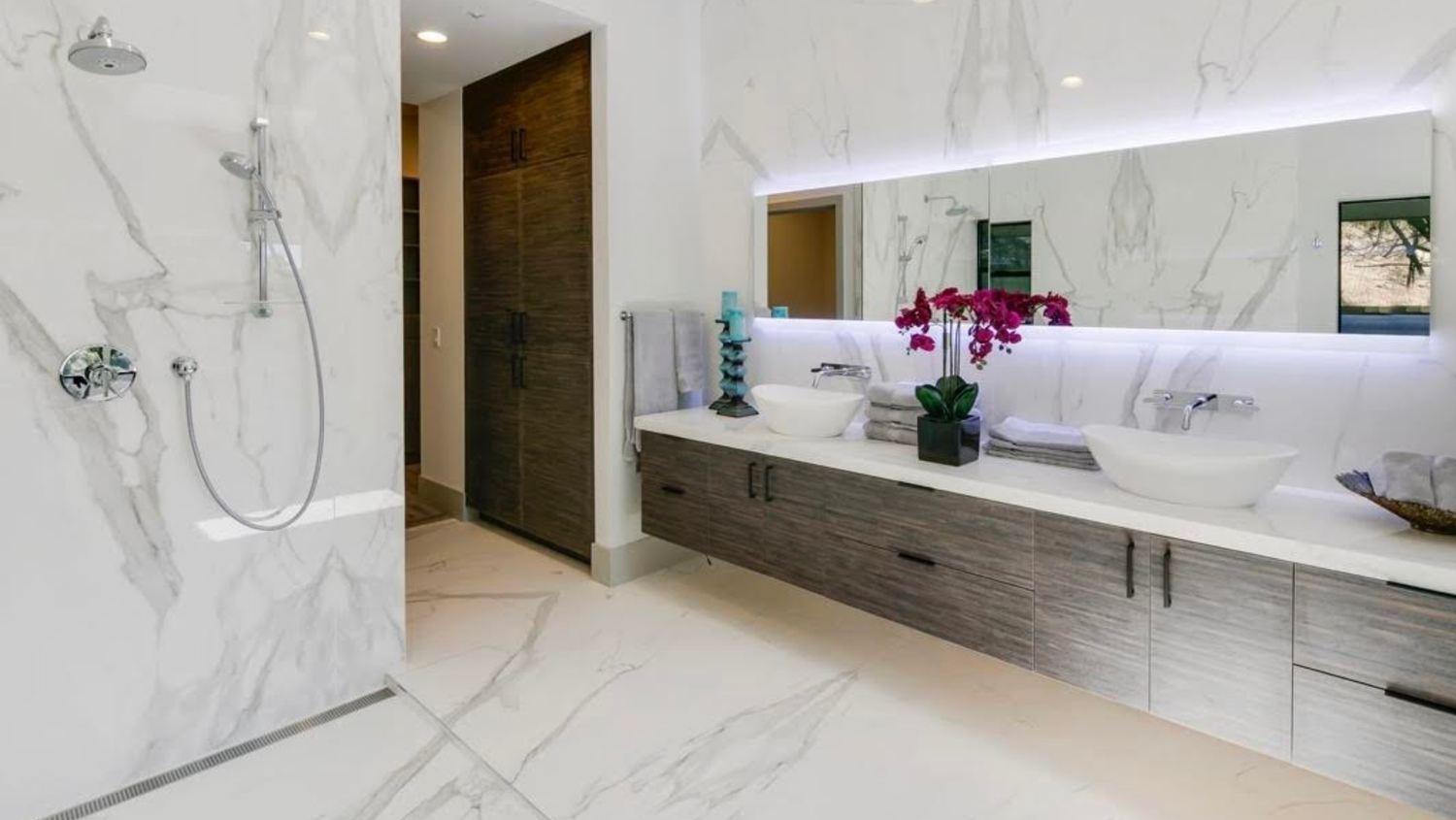 Floating wood bathroom vanity with dual vessel sinks in a marble-tiled bathroom