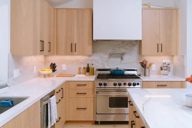 Light wood custom kitchen cabinetry with white countertops and a stainless steel range