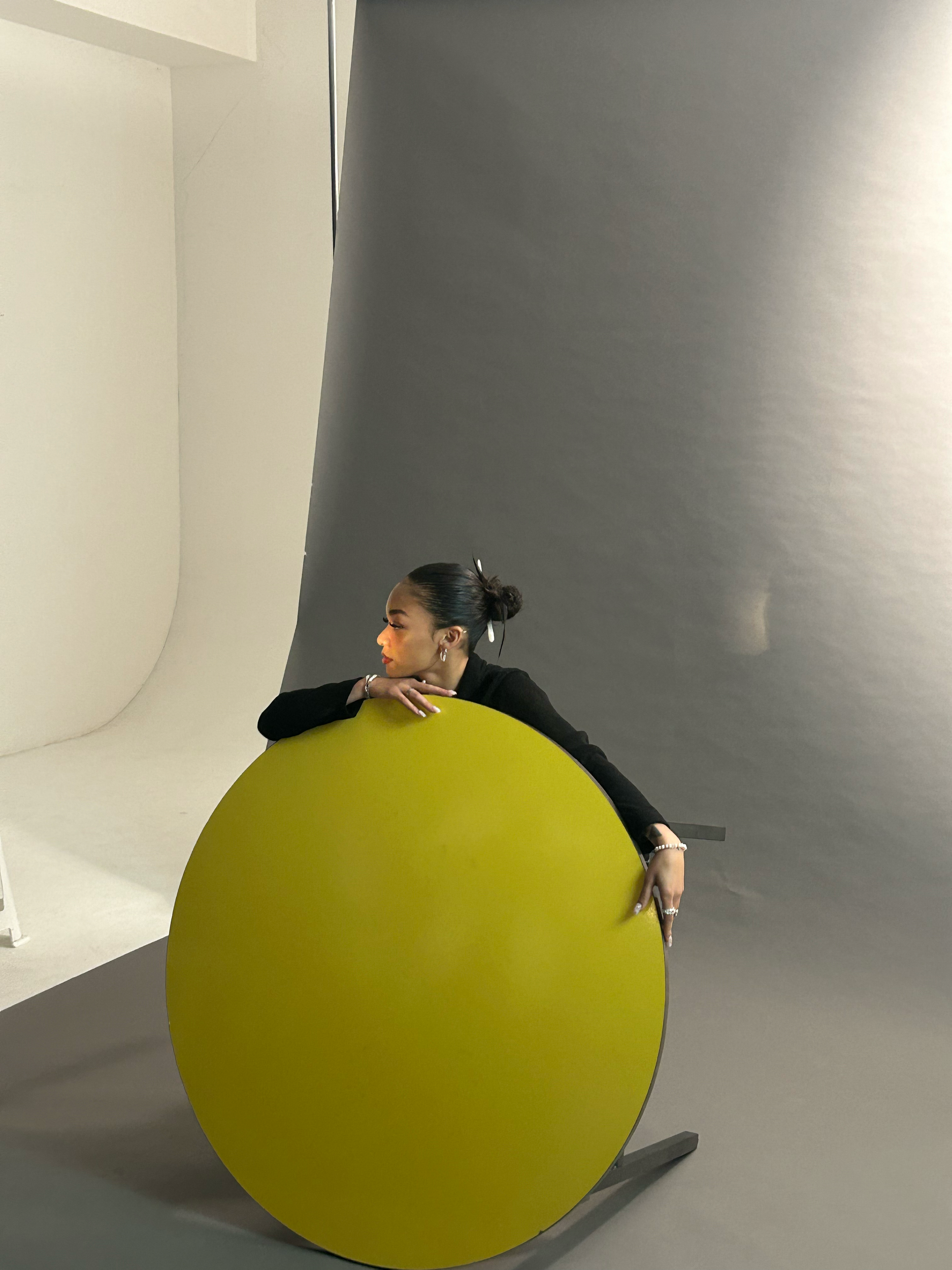 Person partially hidden behind a large green circle on a gray background, with a minimalistic setting designed for photography.