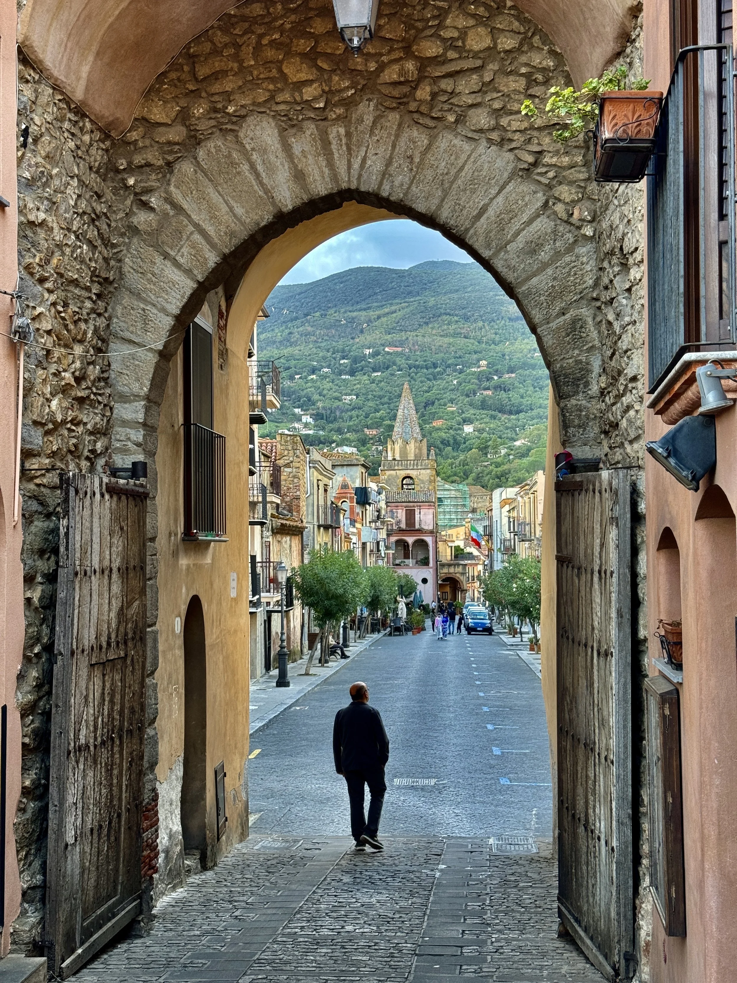 Historic stone archway in Castelbuono Sicily leading to a picturesque street with a distant view of a clock tower and mountainous backdrop.