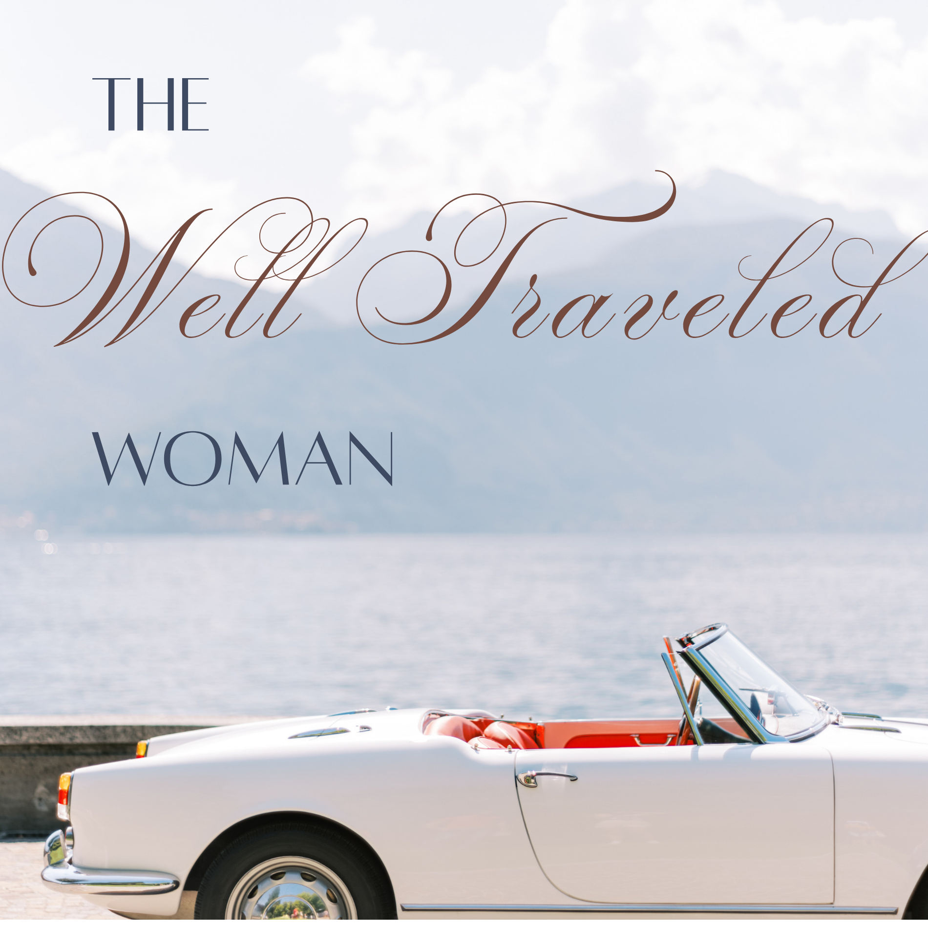A vintage white convertible car parked near a body of water with mountains in the background. The car has red interior details visible through the open top, and there are some books or magazines in the car's dashboard area.