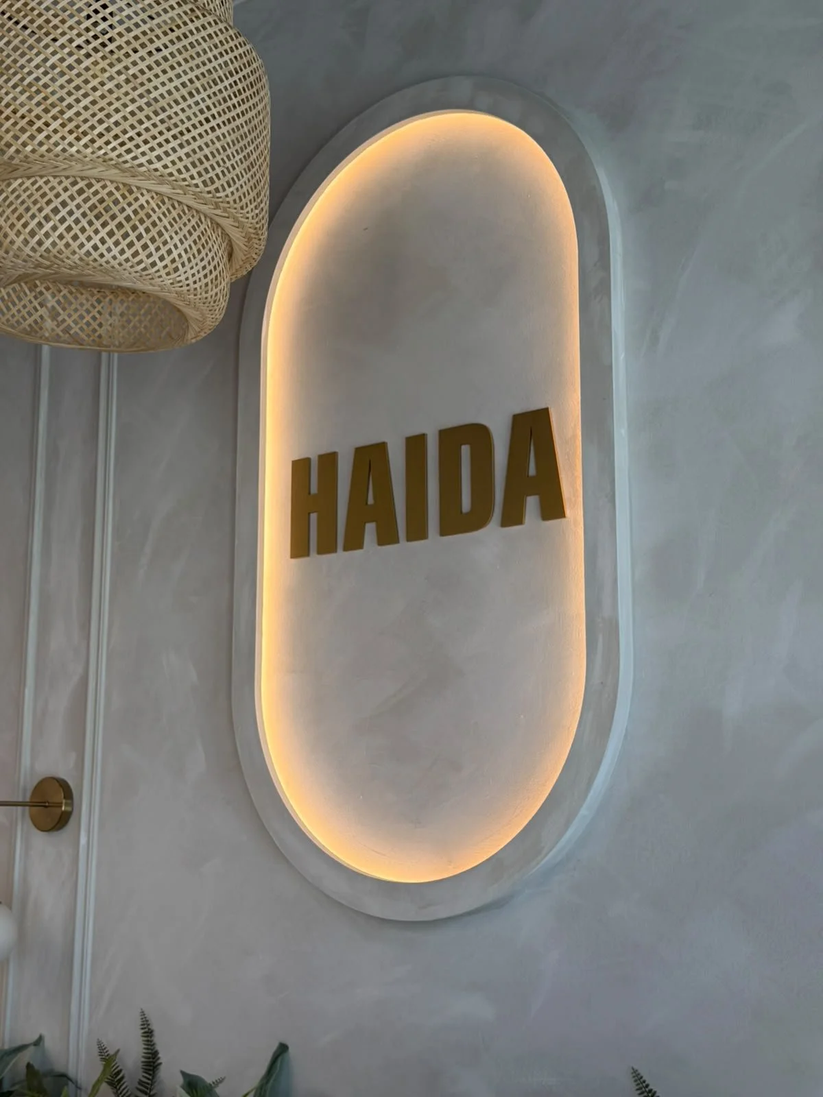 A sign with the word 'HAIDA' in large brown letters on a wall, illuminated by warm backlighting, in a modern interior space.
