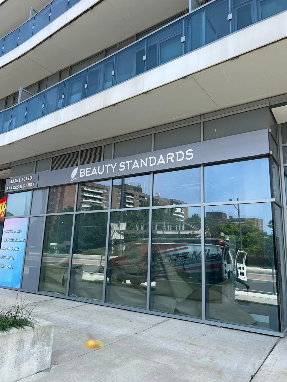 Exterior view of a modern building with large glass windows, showing the store 'Beauty Standards' and signage for 'Rare & Retro Snacks & Candy' and other snacks inside.