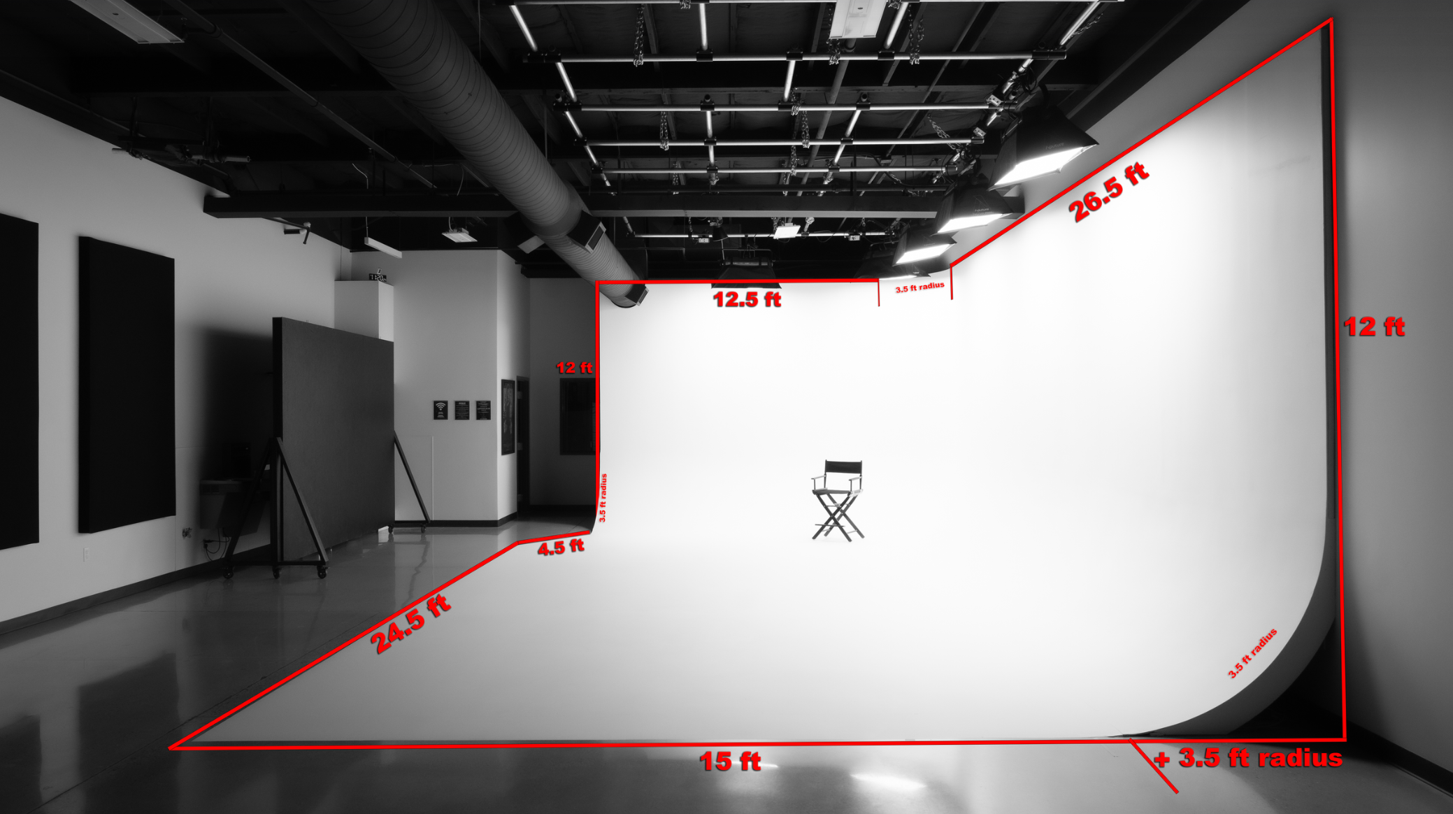 Empty photography studio with a white cyc wall and lighting equipment, measurements marked in red for setting up a photo shoot.