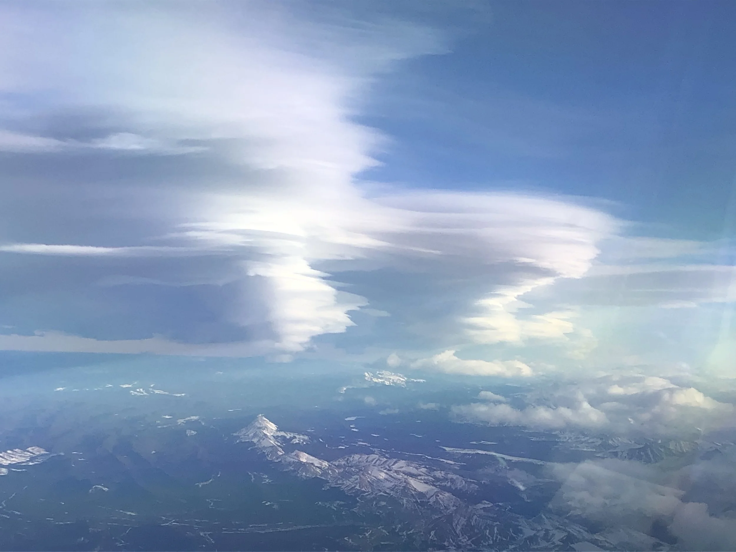 A view of a partly cloudy sky with stacked lenticular cloud and mountain peaks visible at the bottom of the image.