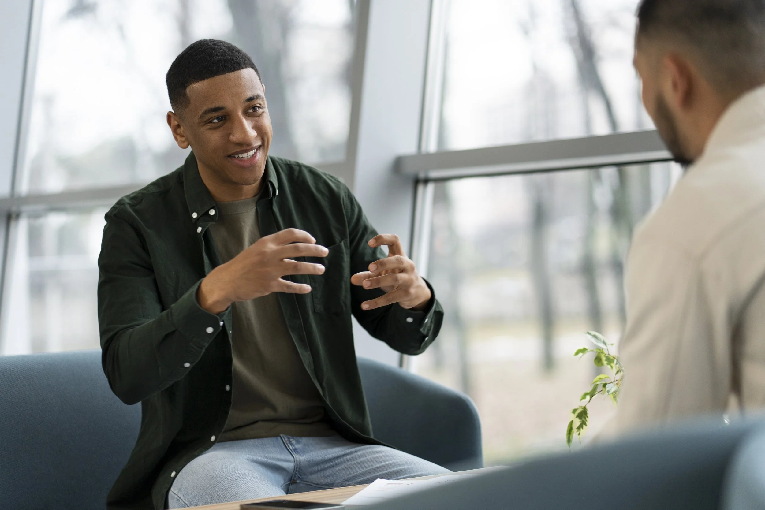 Two men having a conversation in a modern, well-lit room with large windows.