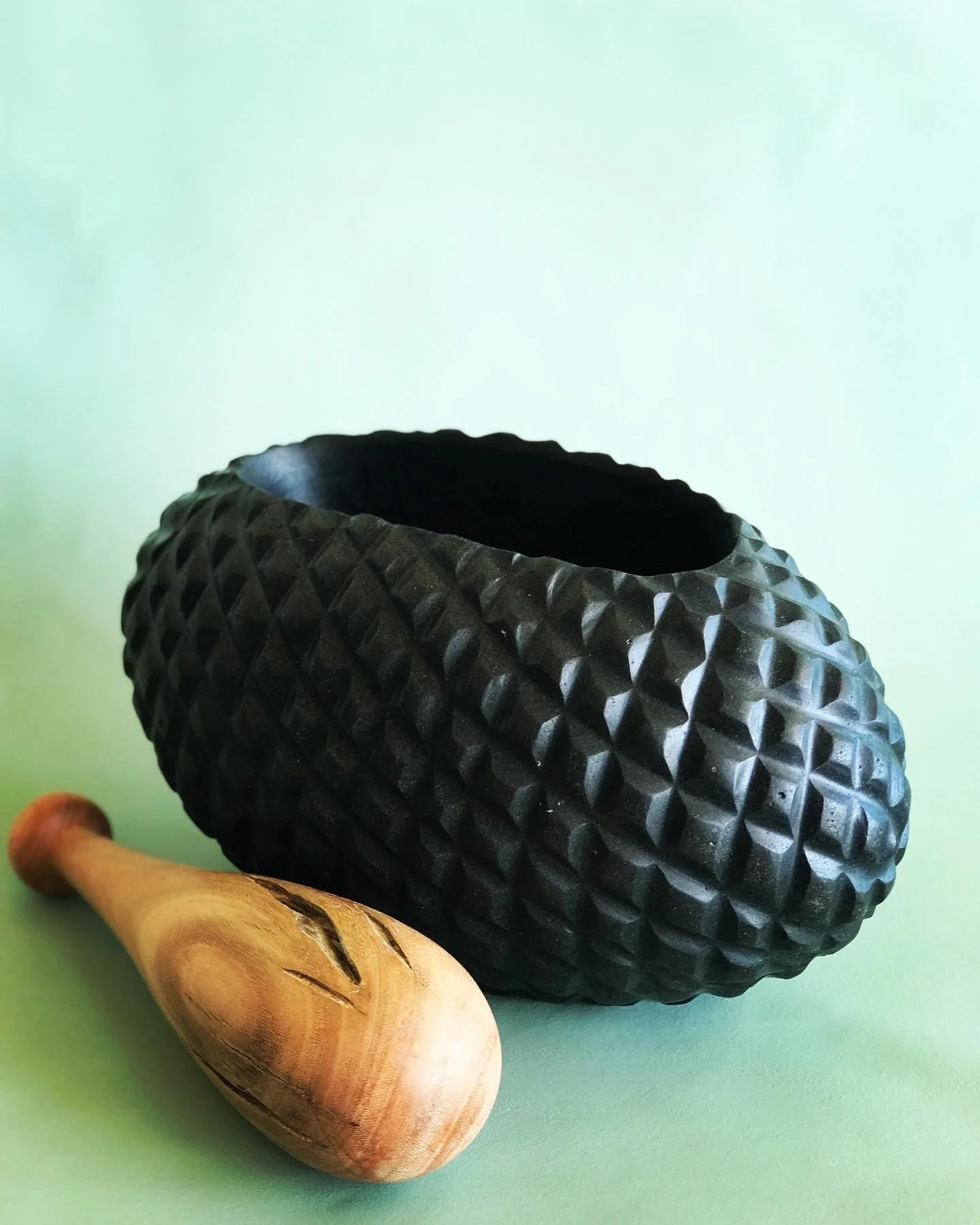 Textured black mortar with wooden pestle on green background.