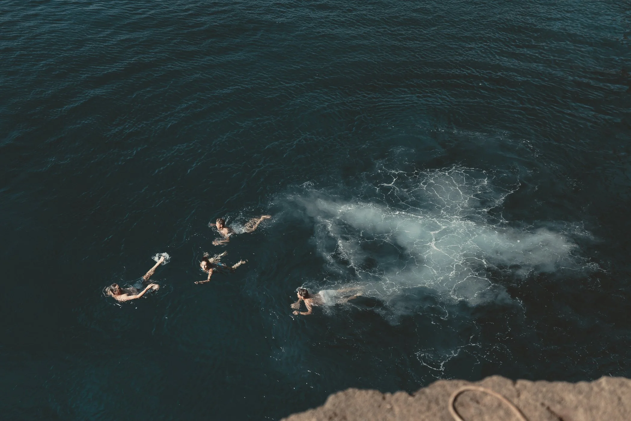 Four people swimming in the ocean near a rocky edge.