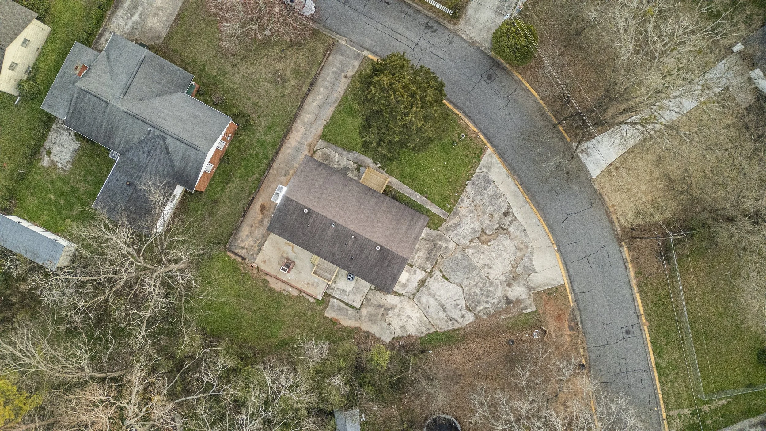 Aerial view of residential houses in Athens, GA with green yards, trees, and a curved street with visible cracks and power lines.