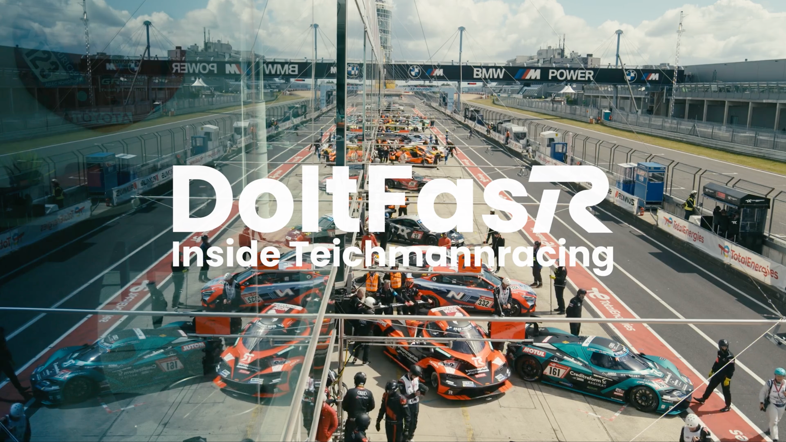 Still from the Do It FasTR documentary: race cars and crew in a motorsport pit lane.