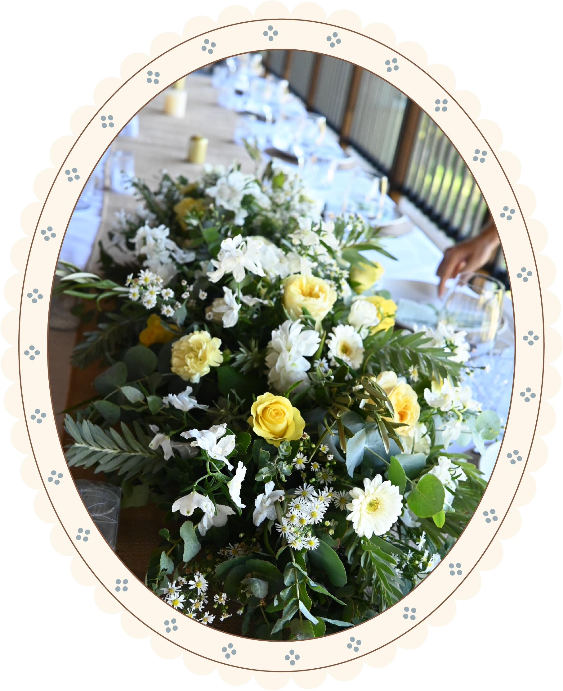 A table decorated with a large floral arrangement consisting of white and yellow flowers, surrounded by glasses, plates, and candles.