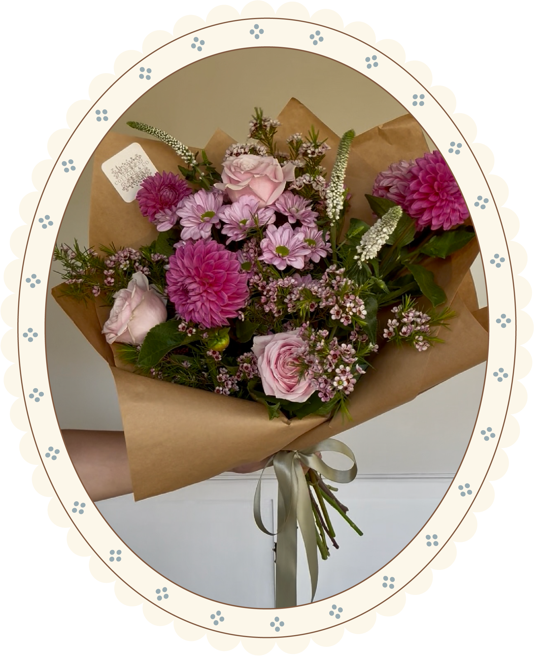 A bouquet of pink and purple flowers wrapped in brown paper and tied with a cream-colored ribbon.
