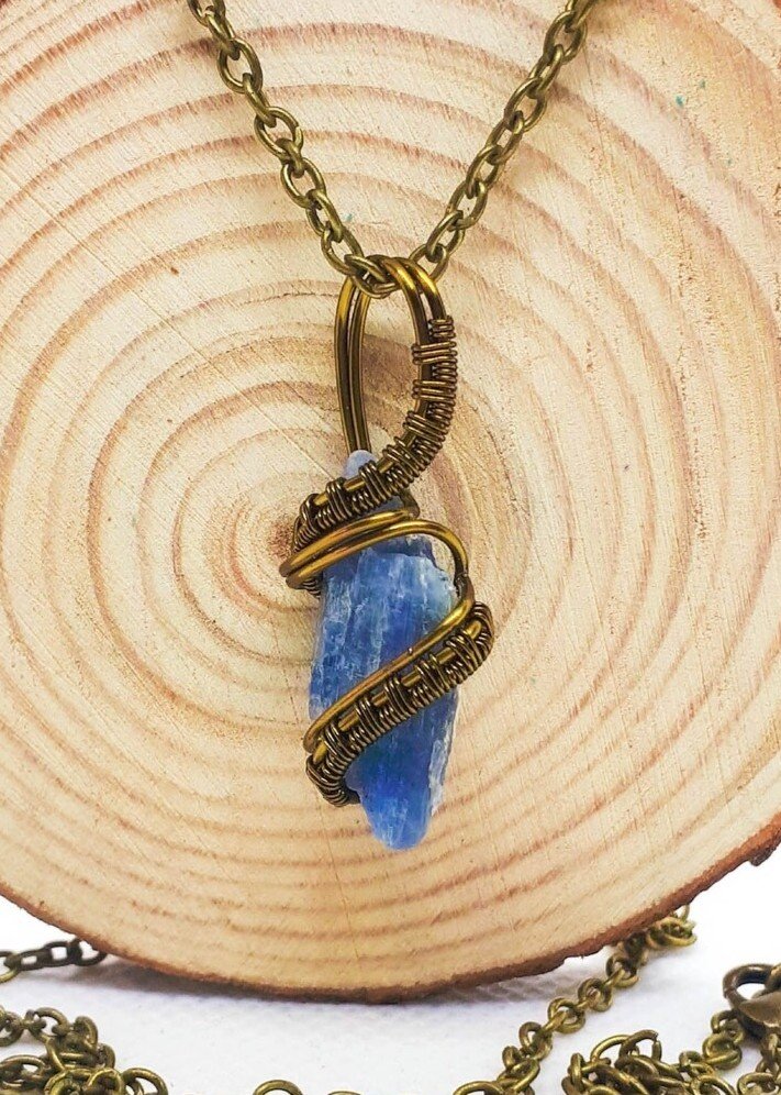 A necklace with a blue kyanite stone pendant wrapped in bronze coloured wire, hanging from a matching chain, displayed against a wooden background.