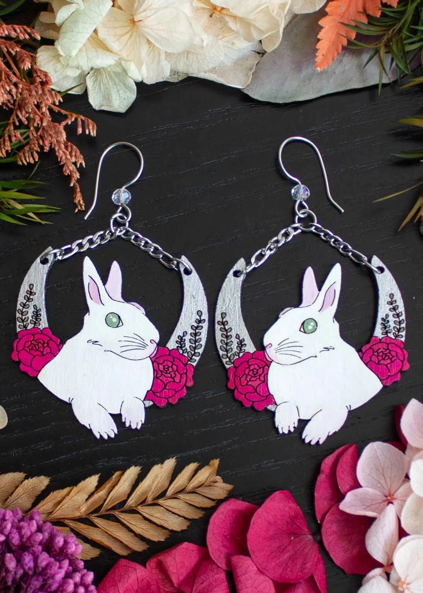 dangle earrings depicting white bannies surrounded by red peonies and leaves sitting atop a silver crescent moon