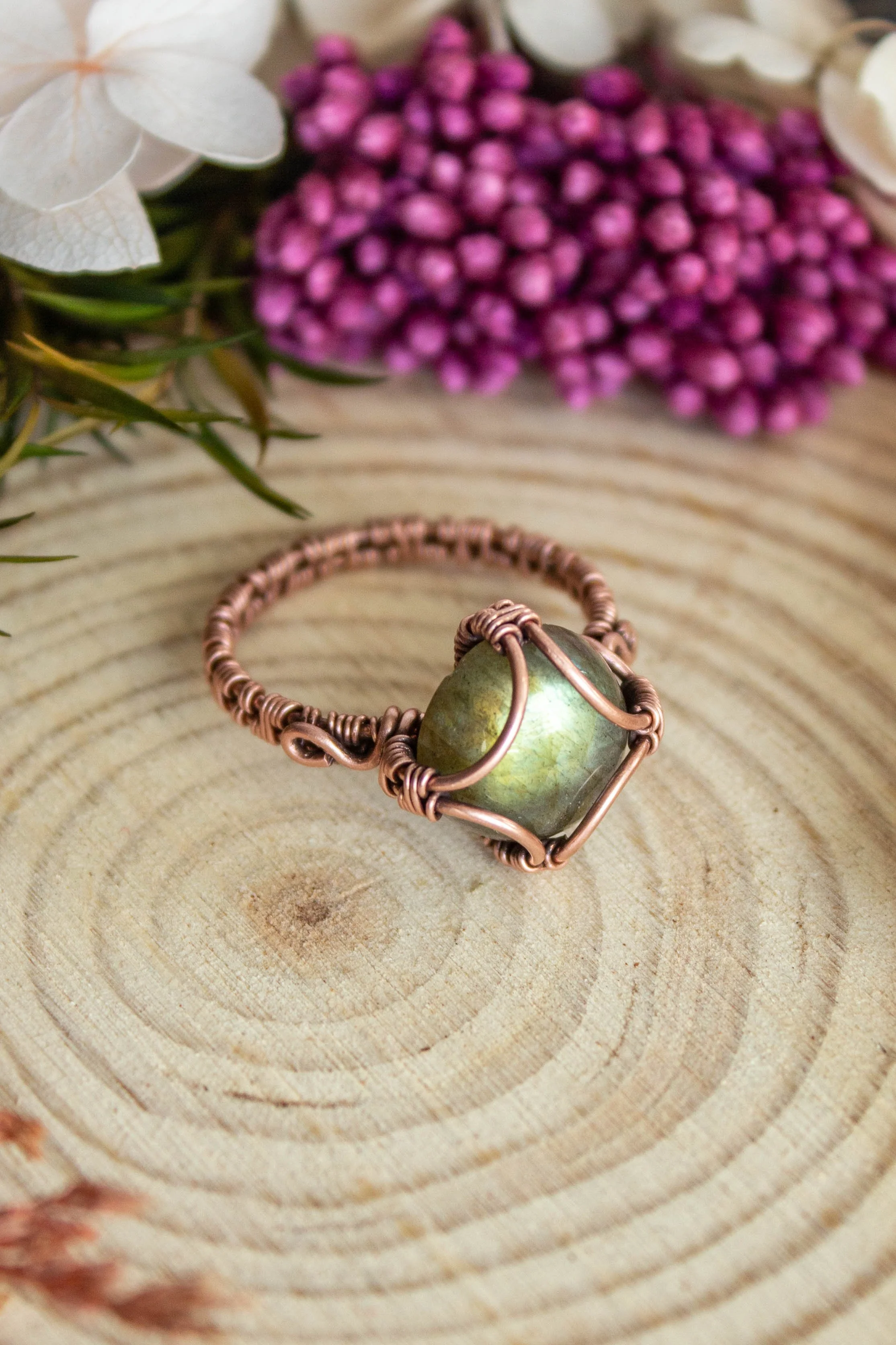 wire wrapped copper ring with round labradorite stone with green flash placed on a wood slice
