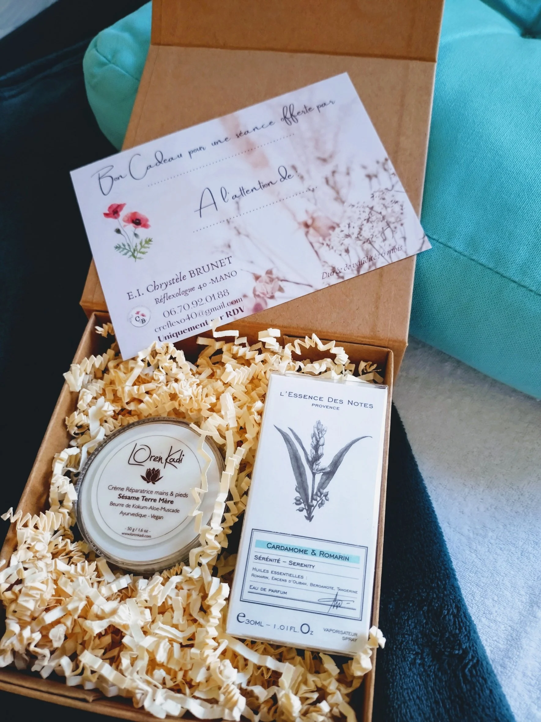 Coffret cadeau contenant une crème pour les mains et pieds et un parfum aux huiles essentielles, le tout dans une boîte contenant du papier de soie, avec une carte cadeau pour une séance de réflexologie.