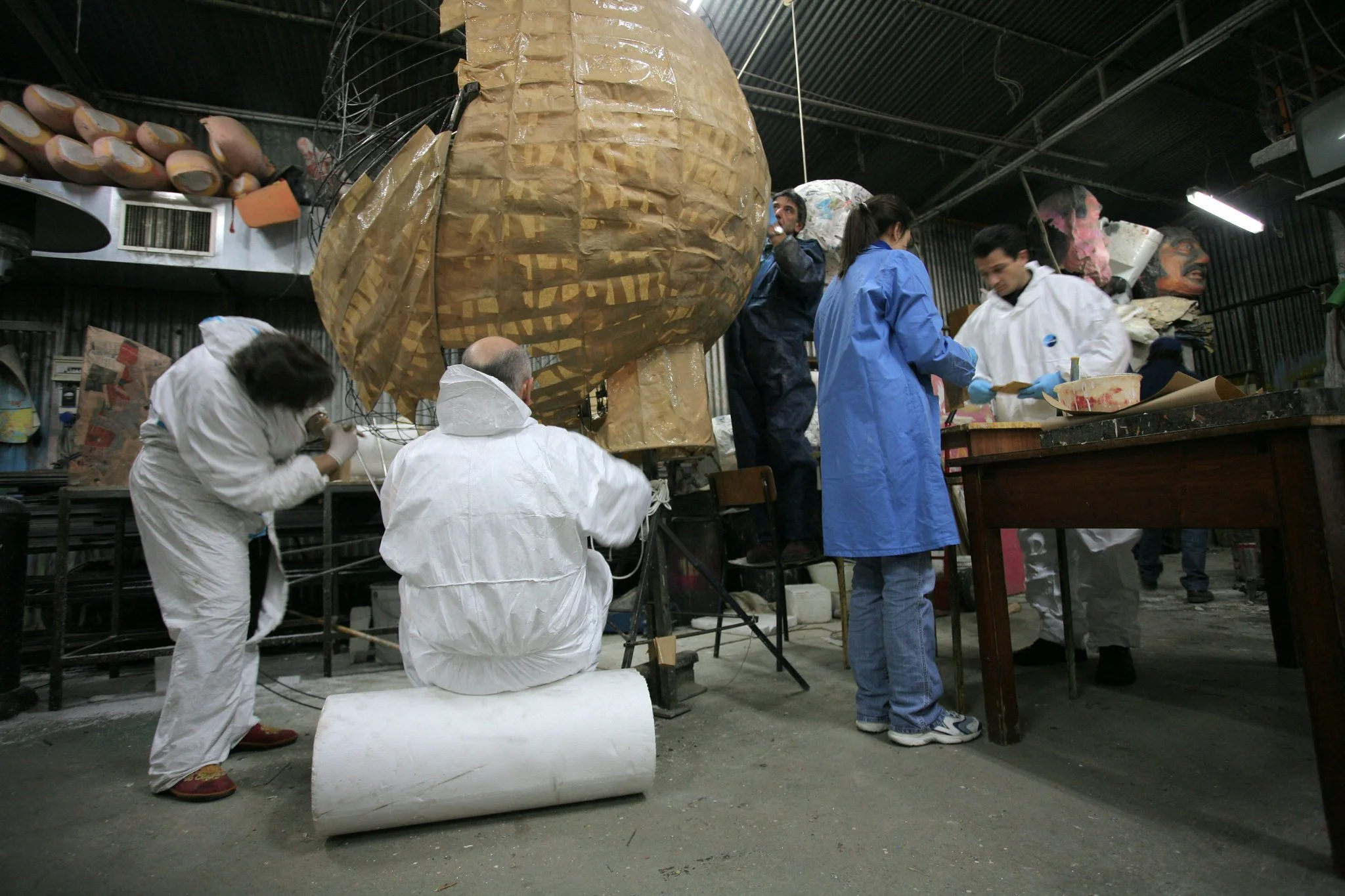 Persone che lavorano su una grande scultura in un atelier, alcune si vestono con tute protettive, una sta seduta mentre altre sono in piedi che collaborano