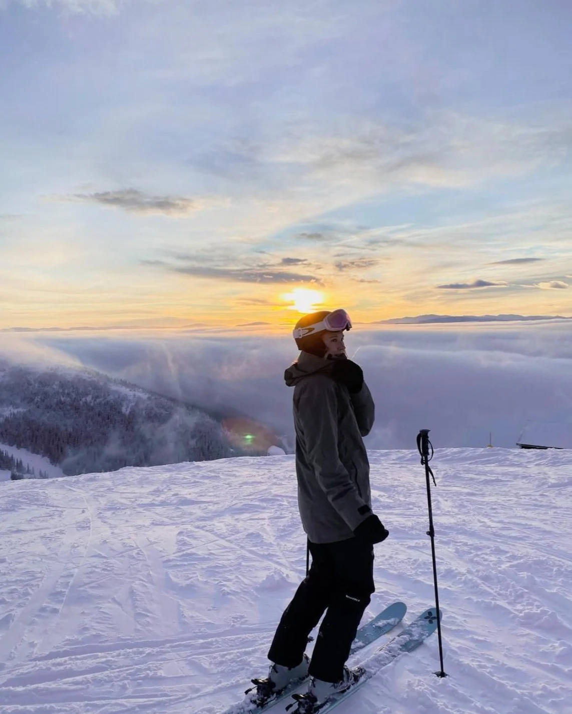 Person i skidhjälm och goggles blickar ut över ett molnhav vid solnedgången på ett snöigt fjäll