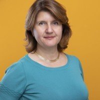 Portrait d'une femme avec des cheveux bruns, portant un t-shirt bleu, devant un fond jaune.