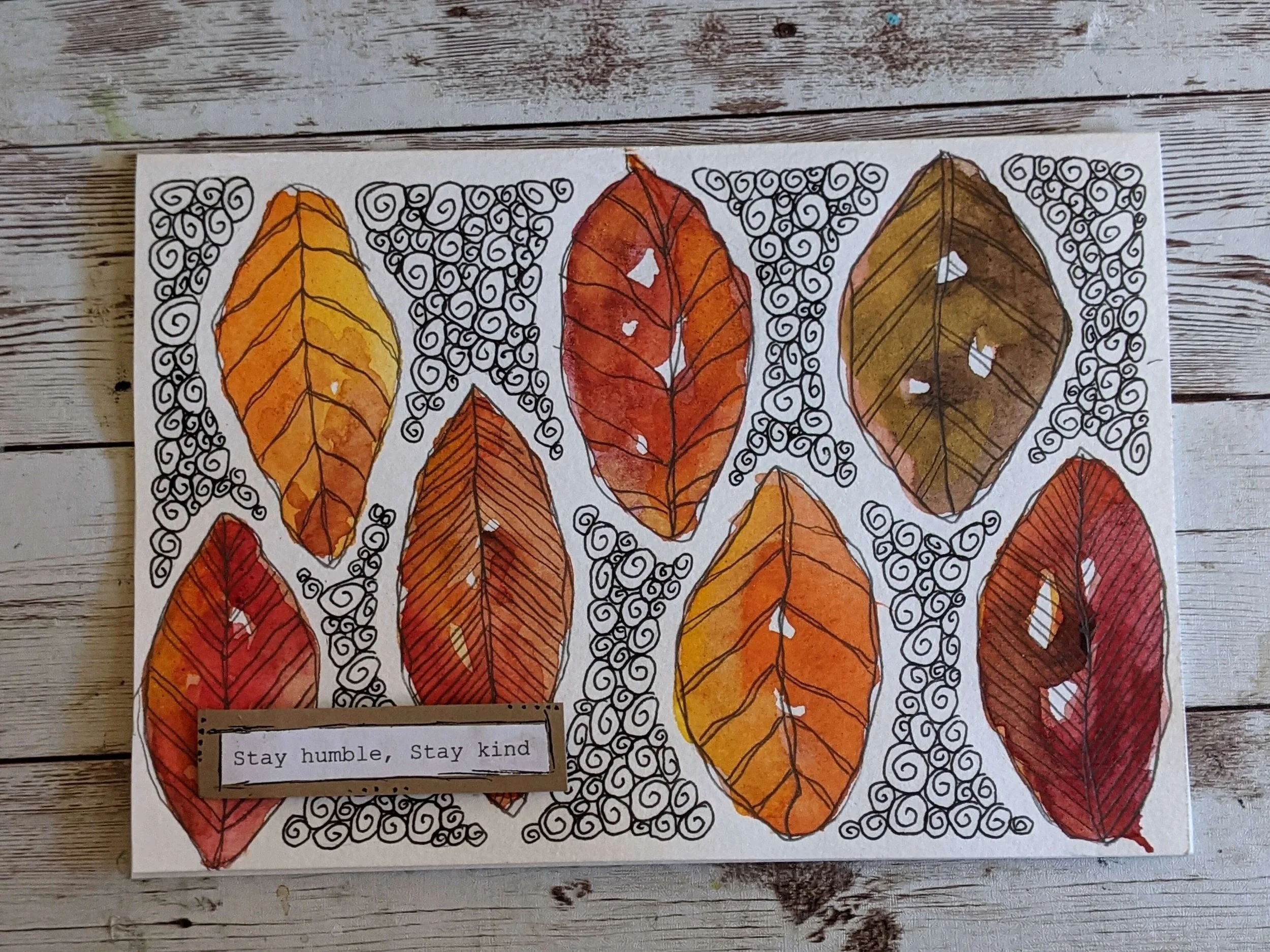 Decorative artwork of various autumn leaves in shades of yellow, orange, red, and brown, outlined in black with intricate swirl and line patterns in the background. A small printed message in the bottom left corner reads, "Stay humble, Stay kind."