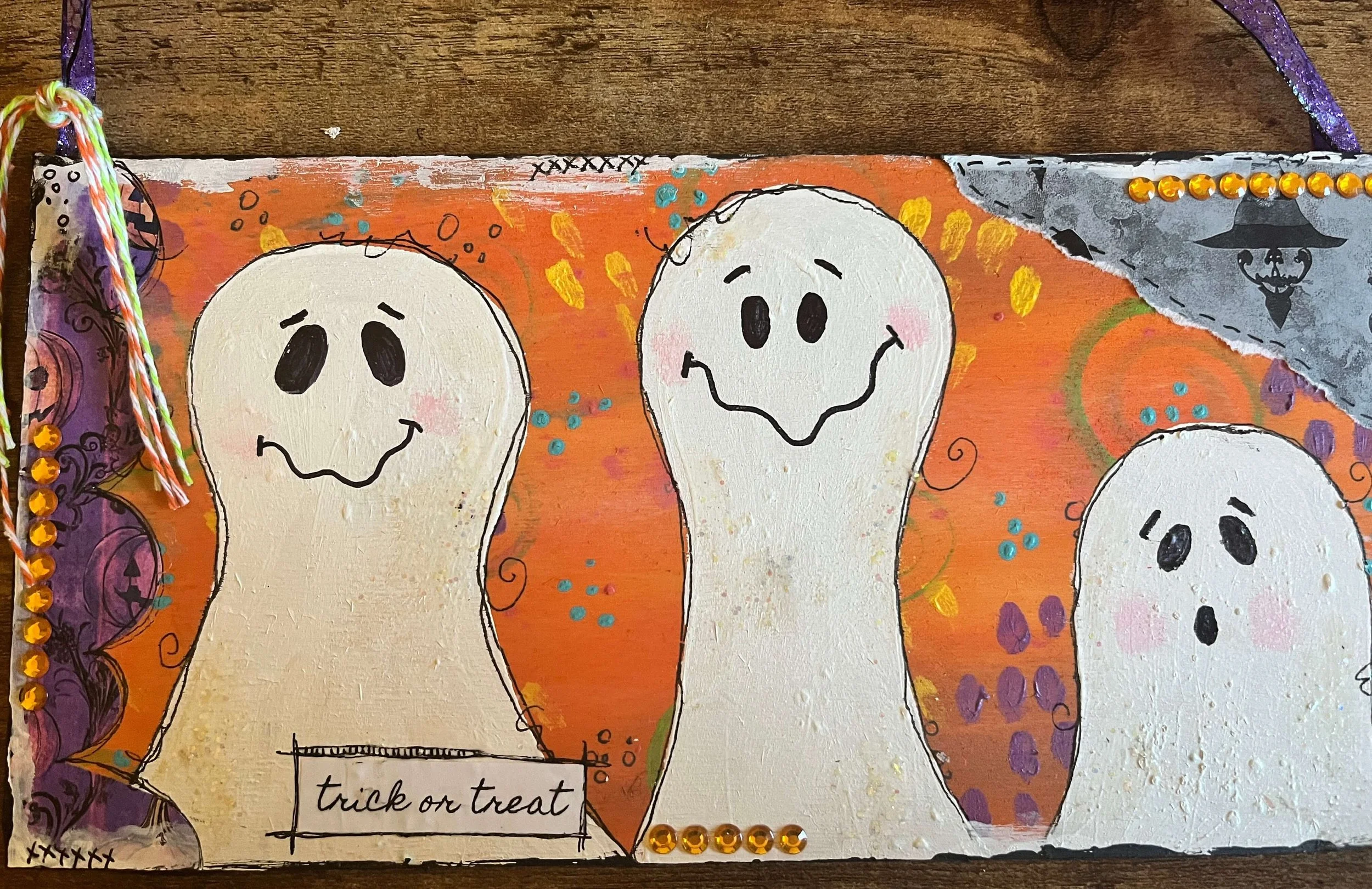 Handmade Halloween card with three smiling ghost illustrations on an orange background, decorated with colorful dots, swirls, and jeweled accents, and labeled 'trick or treat'.