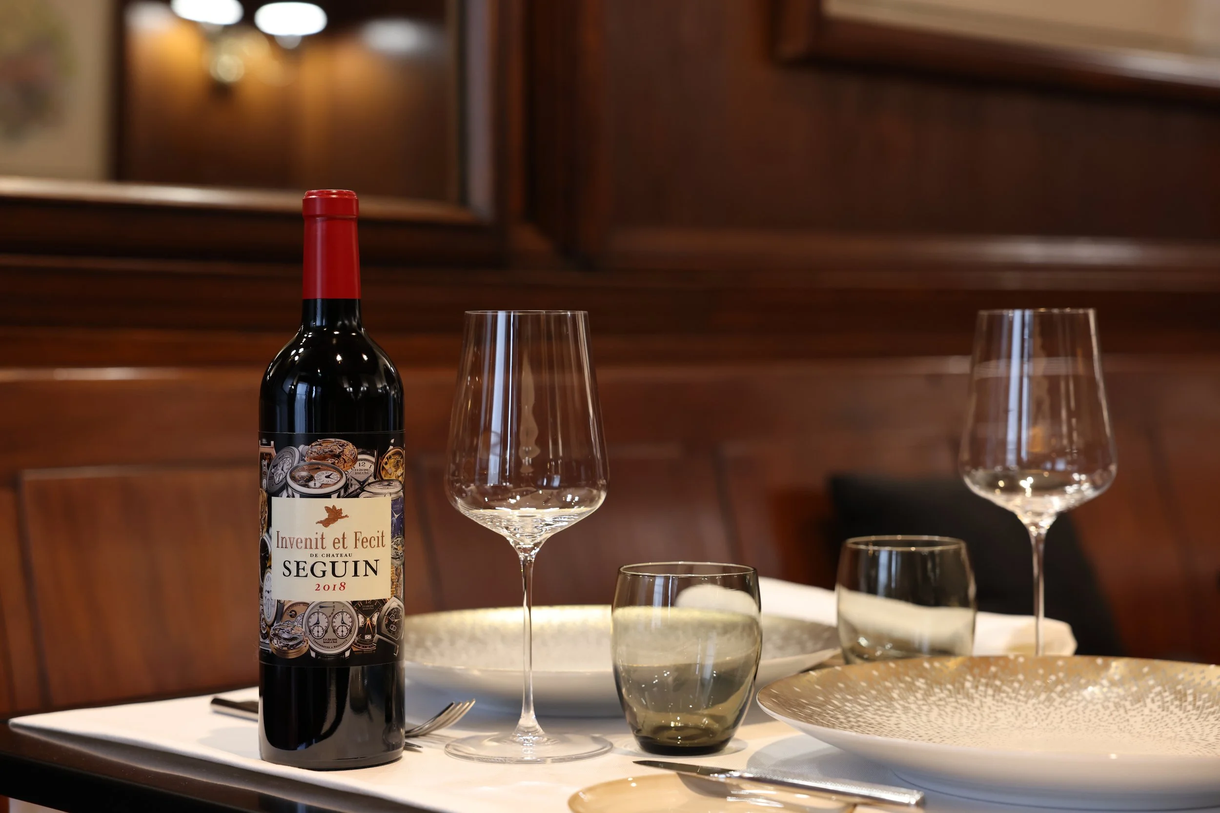 Bottle of "Seguin 2018" red wine on an elegantly laid table with glasses and plates in a restaurant.
