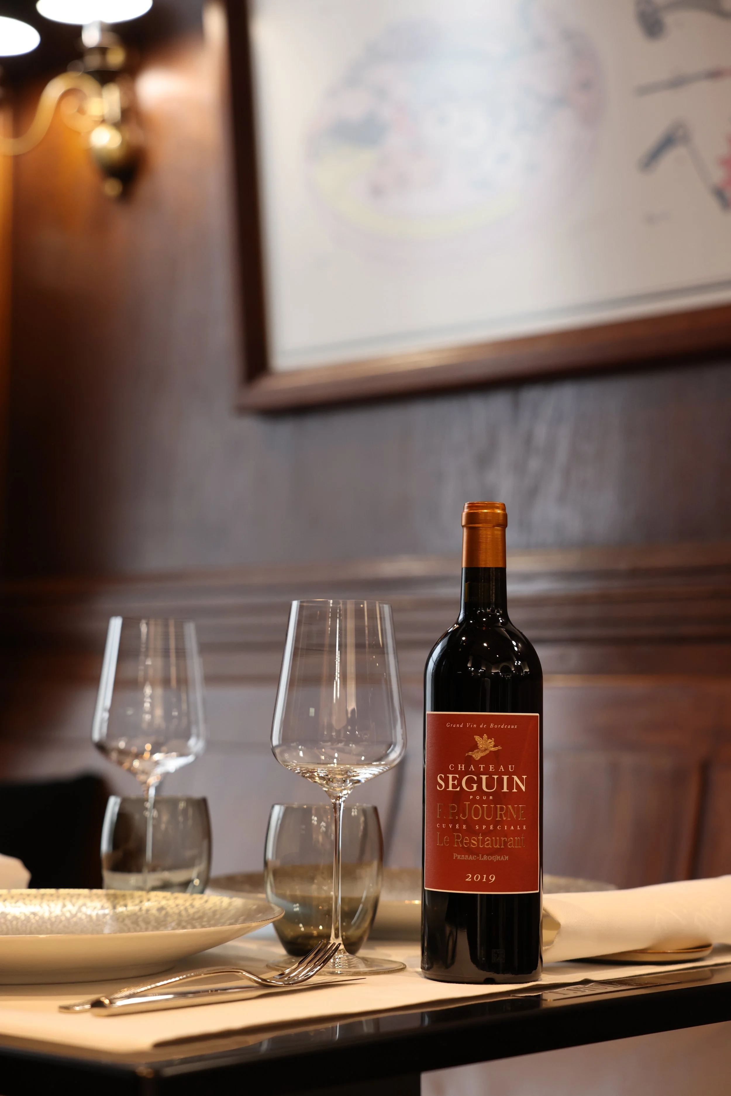 Bottle of Château Seguin wine on an elegant table with two wine glasses and cutlery in a warm restaurant setting.